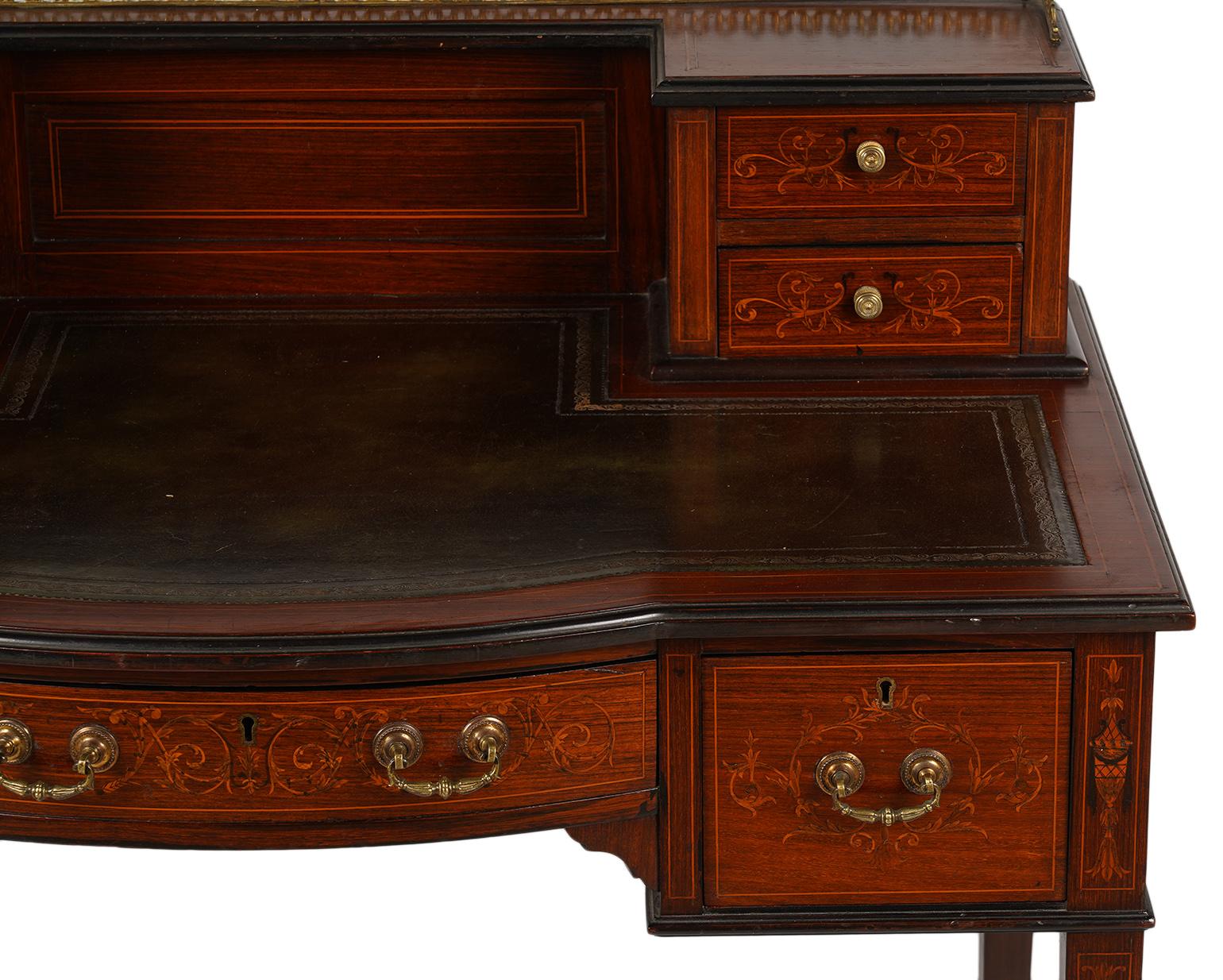 This Edwardian mahogany ladies writing desk is beautifully stringed and inlaid with satinwood. The upper section features a pierced brass top gallery and two drawers on each side. The shaped writing surface is lined with gilt tooled leather above a