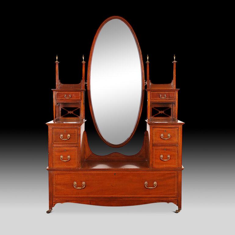 An English inlaid mahogany vanity or dressing table with a large oval mirror and multiple drawers of a variety of sizes. C. 1910