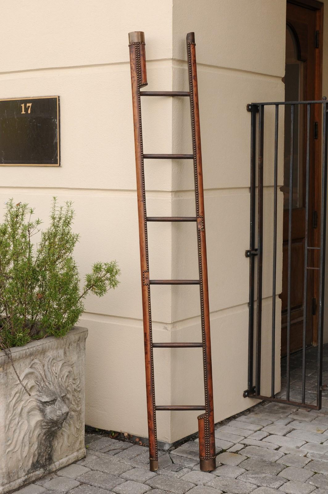An English Edwardian leather covered wooden folding ladder from the early 20th century, with nailhead trim. Born during the first quarter of the 20th century, this folding ladder features a rounded wooden structure covered with brown leather,