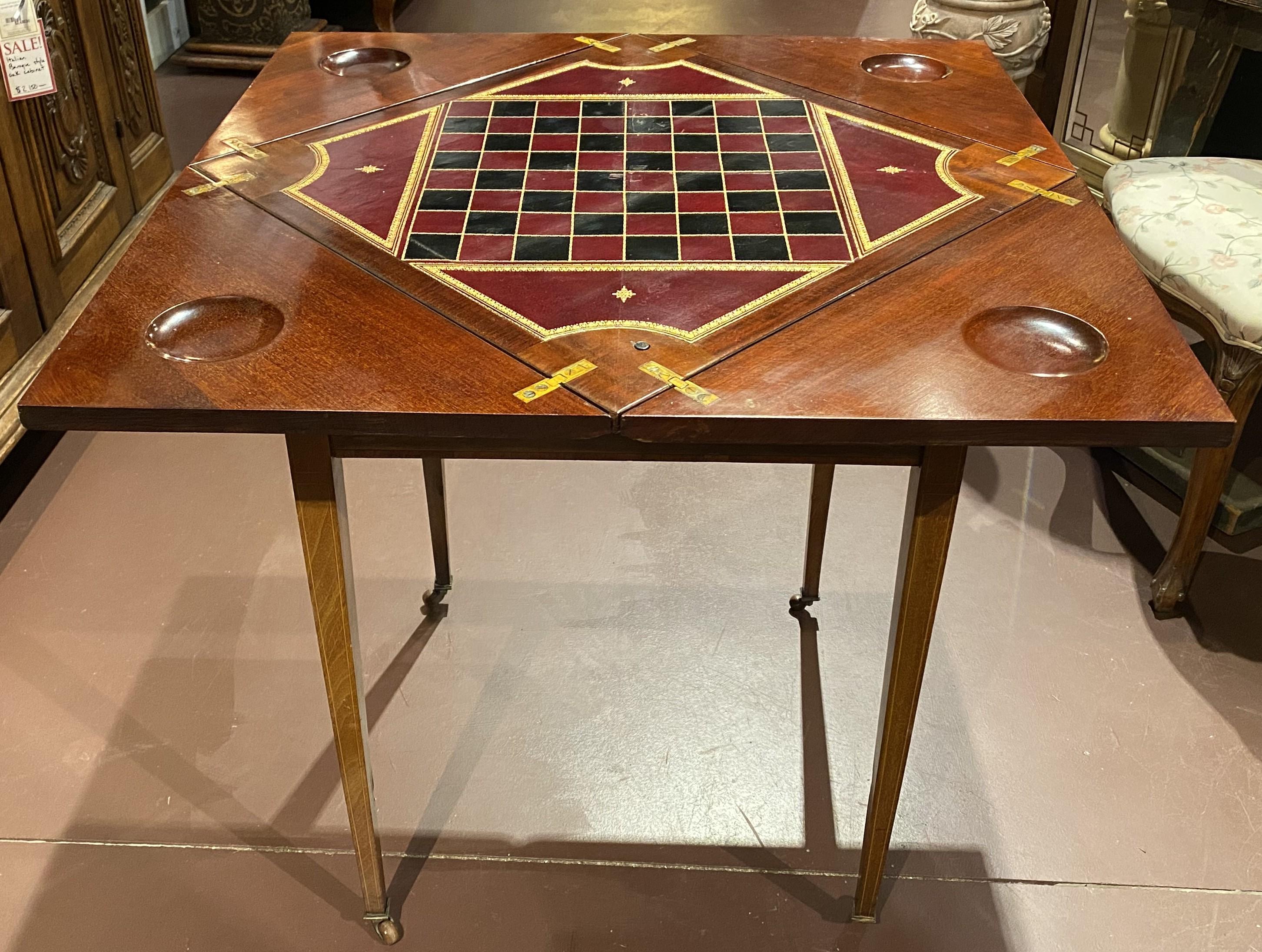 A fine English Edwardian mahogany games table with folding handkerchief top, opening to a tooled leather gaming chess or checker board, counter wells on each corner, satinwood border and line inlay, felted corners, over a conforming frieze with a