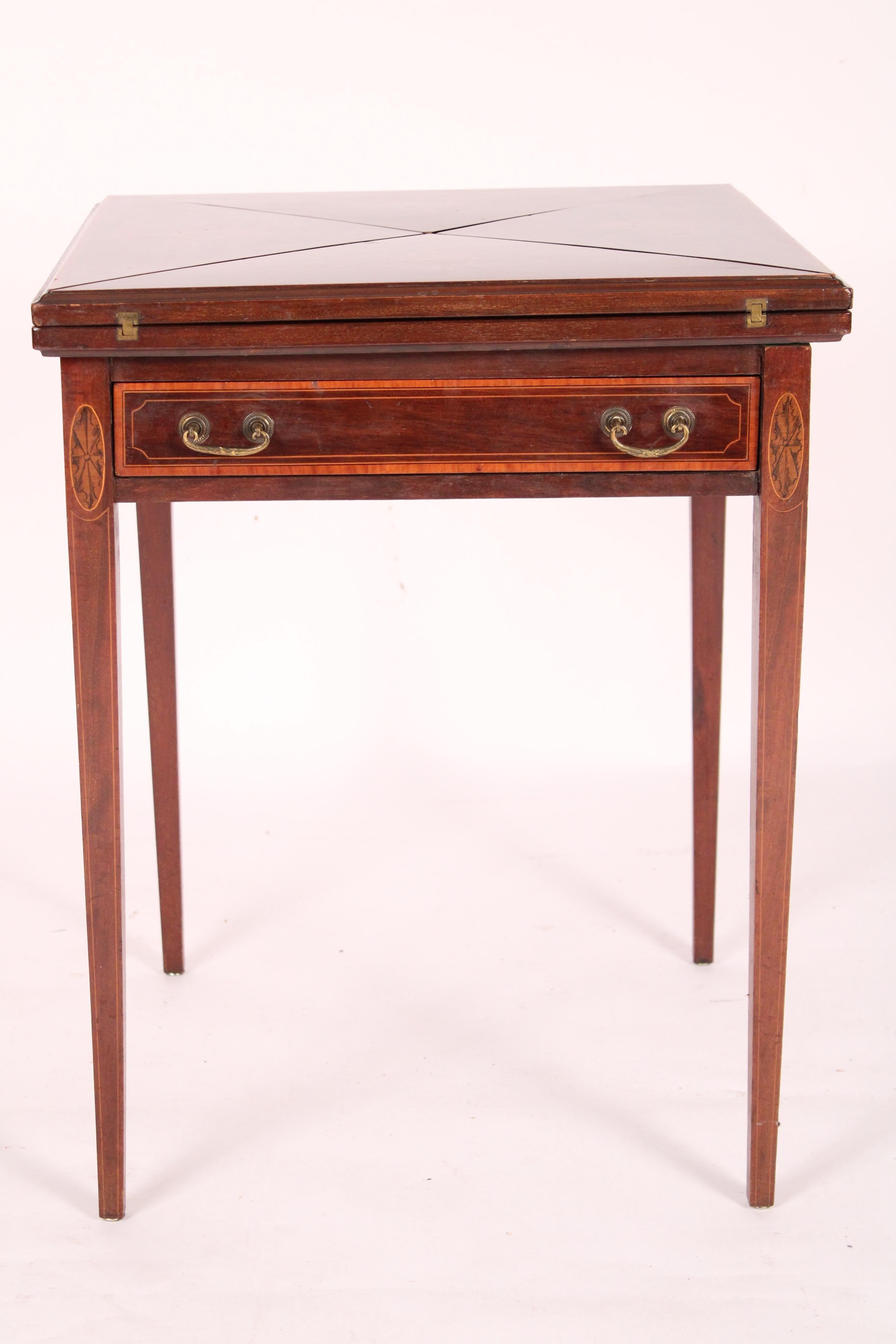 English Edwardian mahogany napkin fold top games, circa 1910. With a mahogany napkin fold top with tulip wood crossbanding, each triangular section with inlaid cartouche, when opened there is a tooled leather playing surface,  each triangular