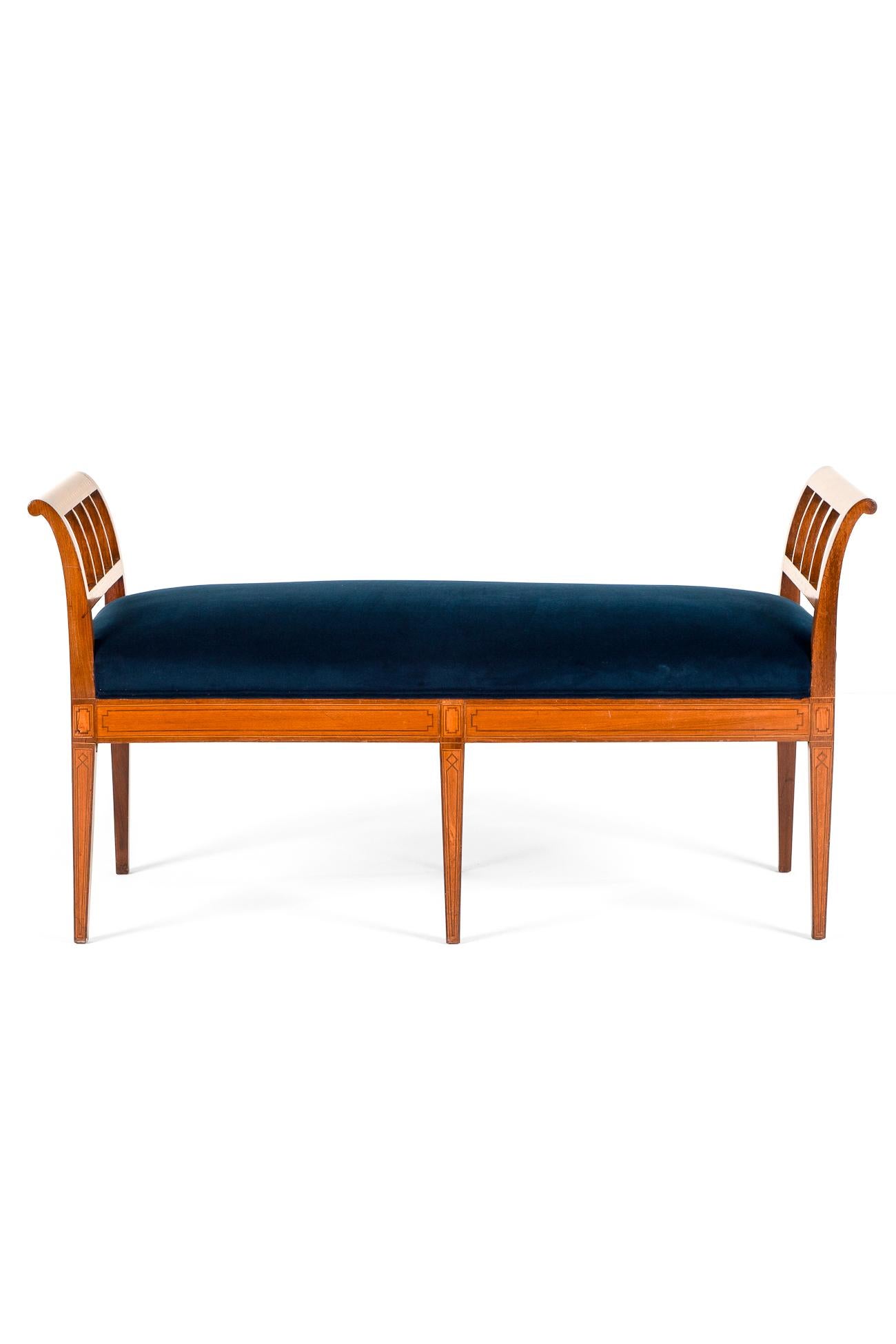 A charming Edwardian mahogany rectangular window seat inlaid with decorative satin wood inlays and floral motifs.

With two scroll ends with parallel upright supports accompanied with a freshly reupholstered navy velvet seat.

All raised on six
