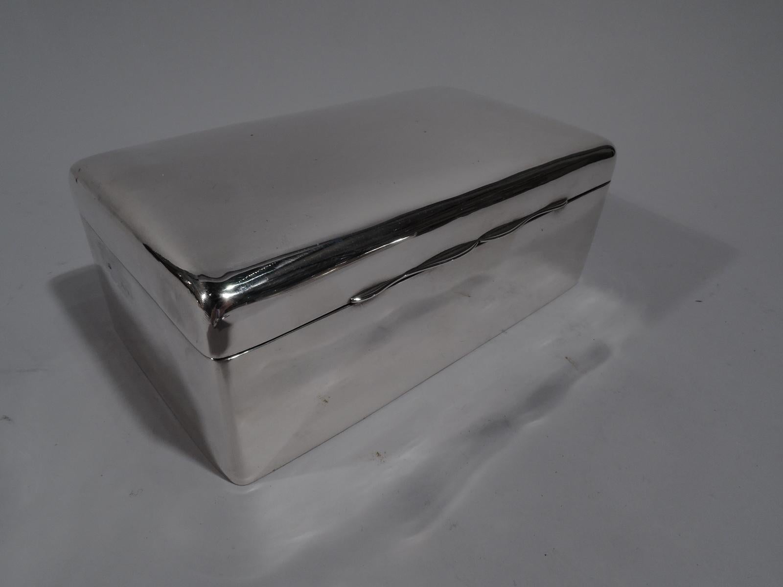 Edwardian Modern sterling silver box. Rectangular with curved corners. Cover flat and hinged with elegant double-scroll tab. Box interior cedar lined and partitioned. Underside leather lined. Cover interior gilt washed. Fully marked with maker’s