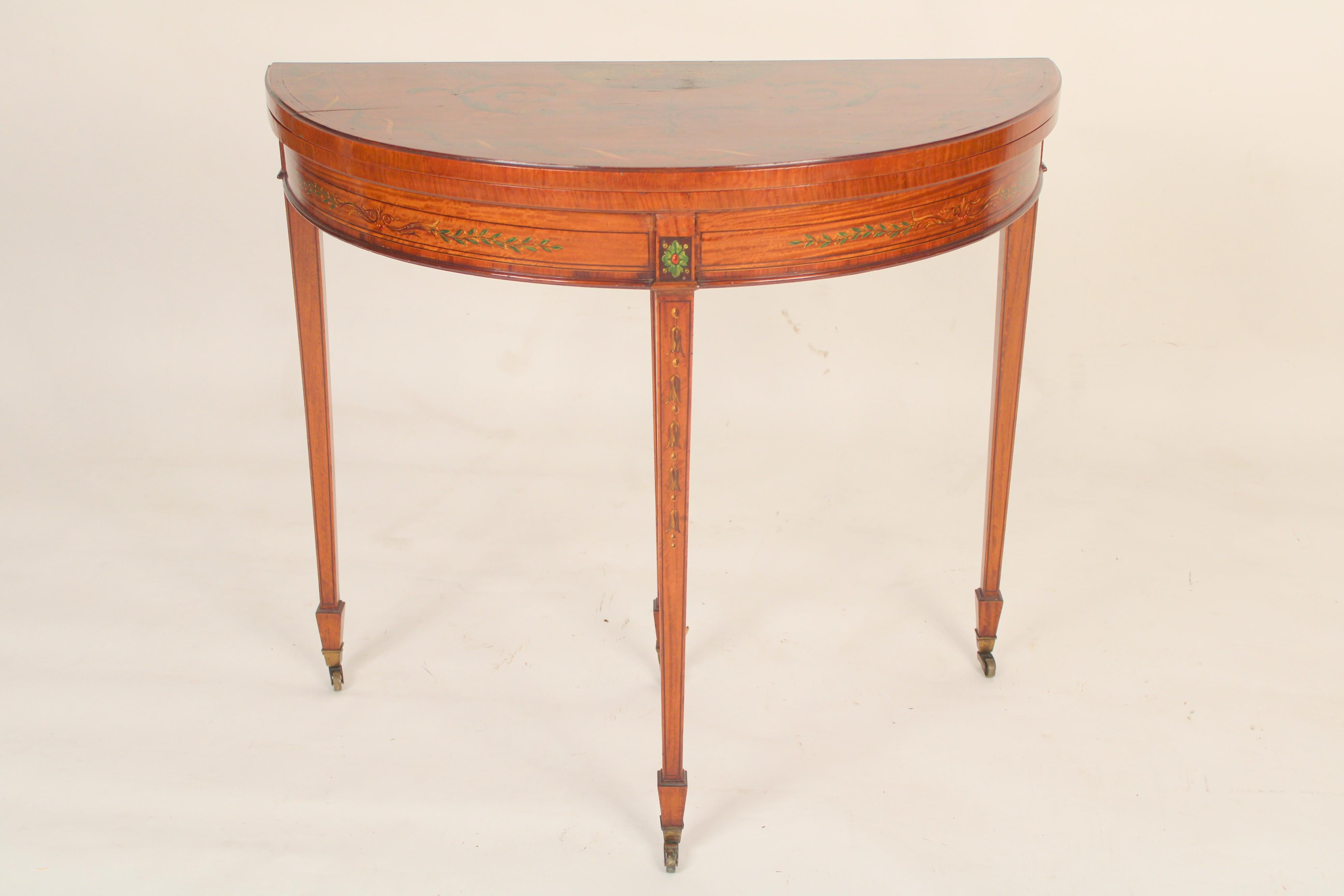 Englischer edwardianischer Demi-Lune-Tisch aus satiniertem Holz, um 1900. Der Deckel der Demi Lune ist mit einer Gruppe von Amoretten und Ranken bemalt. Der Fries ist mit wallenden Ranken bemalt. Die quadratischen, konischen Beine sind mit