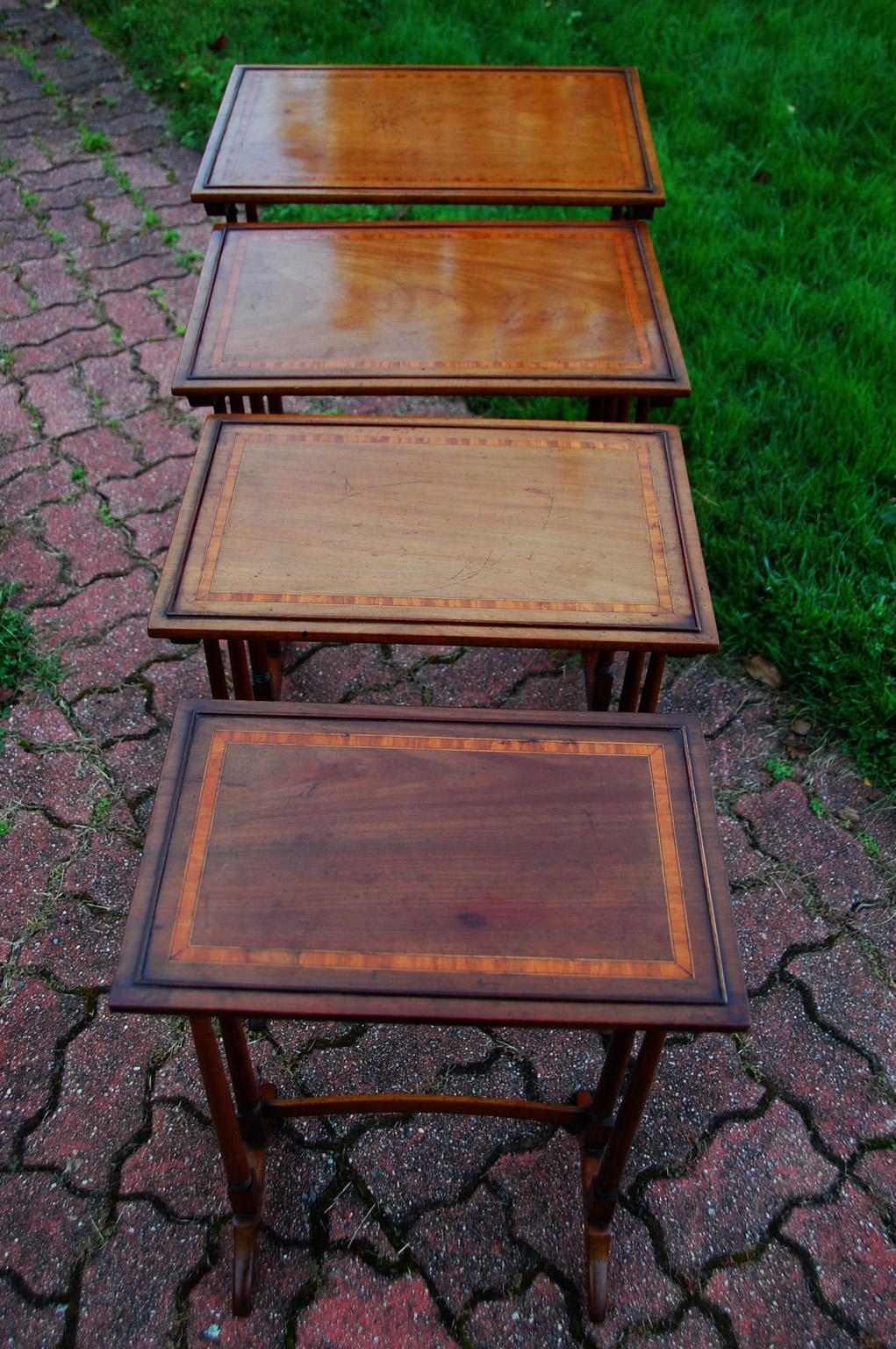 English Edwardian period nest of four tables. These mahogany tables have satinwood crossbanding enclosed by delicate boxwood and ebony stringing with a low simple gallery on each table. These are all in good condition, but the topmost table