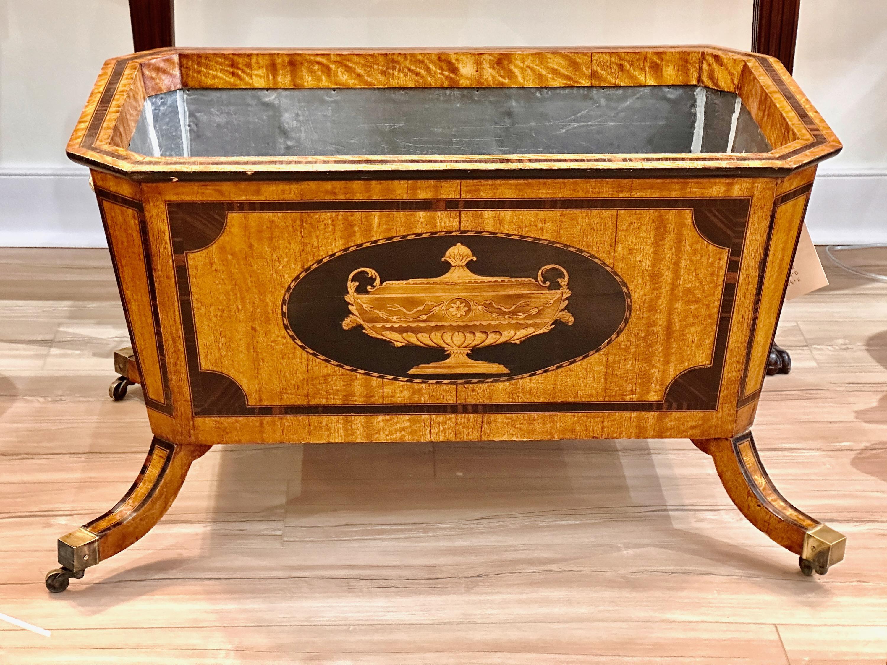 An early 20th century English Edwardian Regency style mahogany and satinwood zinc lined wine cooler or planter resting on splayed legs terminating in brass casters with large brass handles on either end.