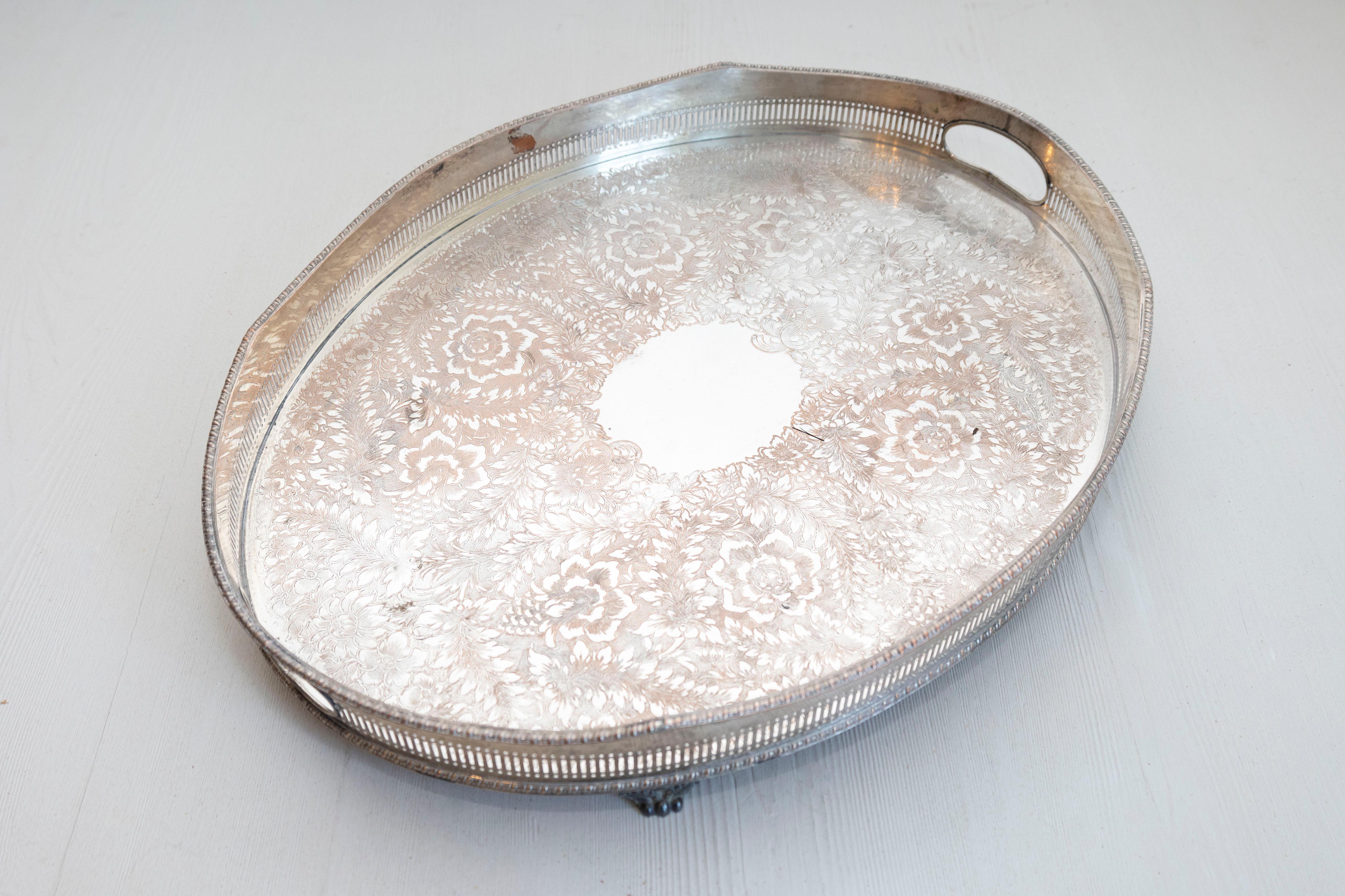 An English Edwardian period oval silver plated tray from the early 20th century, with pierced border, floral motifs and petite scrolling feet. Born in England in the early years of King Edward VII's reign, this exquisite silver plated tray features