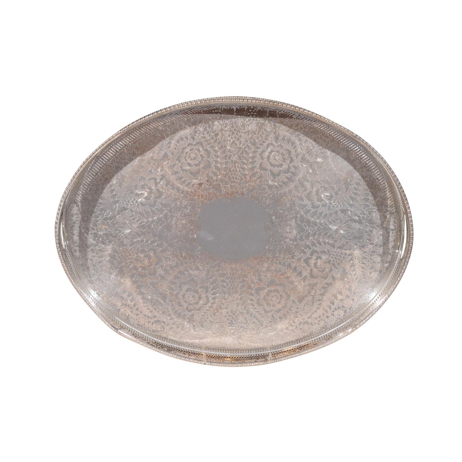 An English Edwardian period oval silver plated tray from the early 20th century, with pierced border, floral motifs and petite scrolling feet. Born in England in the early years of King Edward VII's reign, this exquisite silver plated tray features