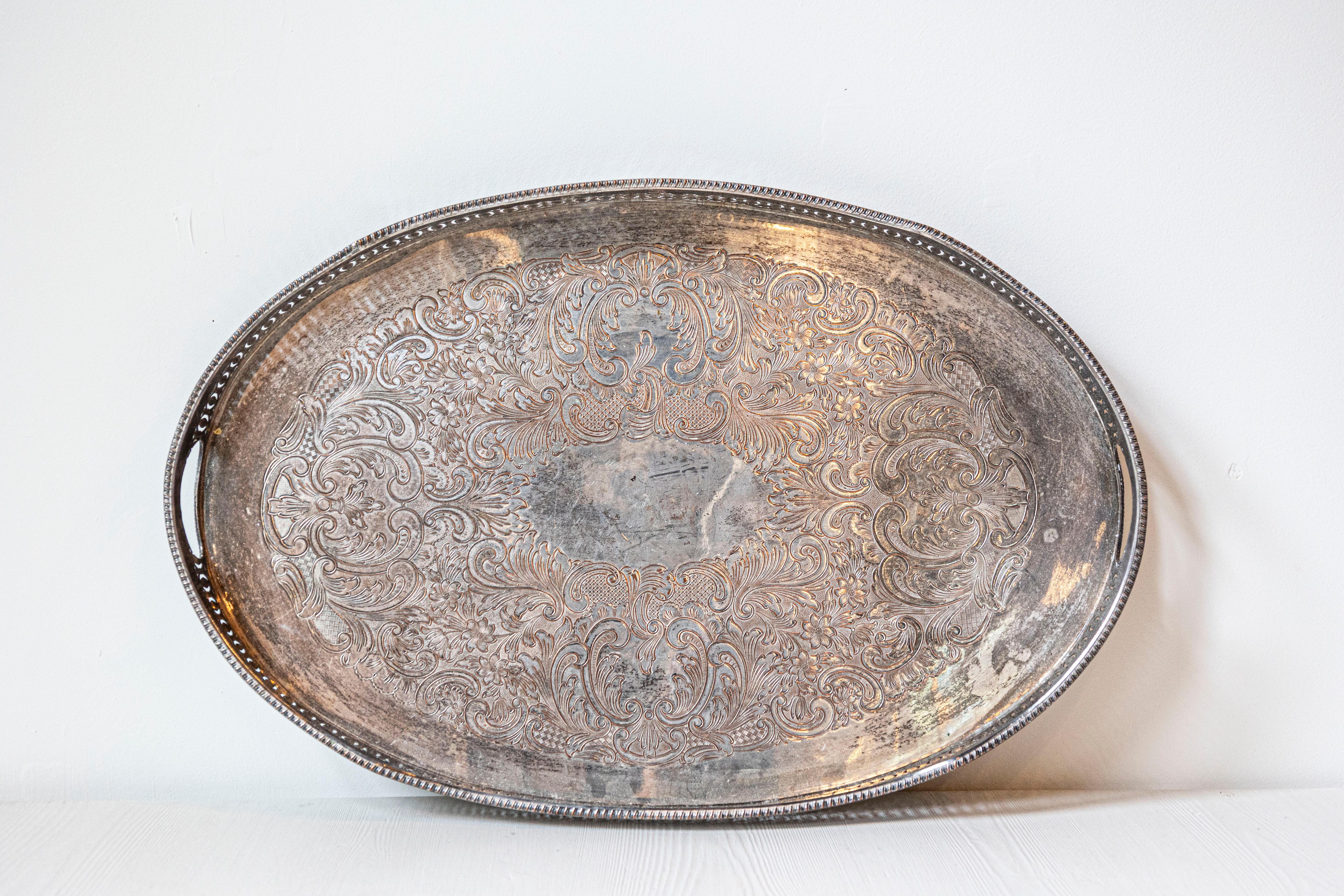 Bandeja inglesa de principios del siglo XX bañada en plata de la época eduardiana, con motivos calados, diseño de volutas en C y pátina oxidada. Nacida en Inglaterra en los primeros años del reinado de Eduardo VII, esta exquisita bandeja bañada en