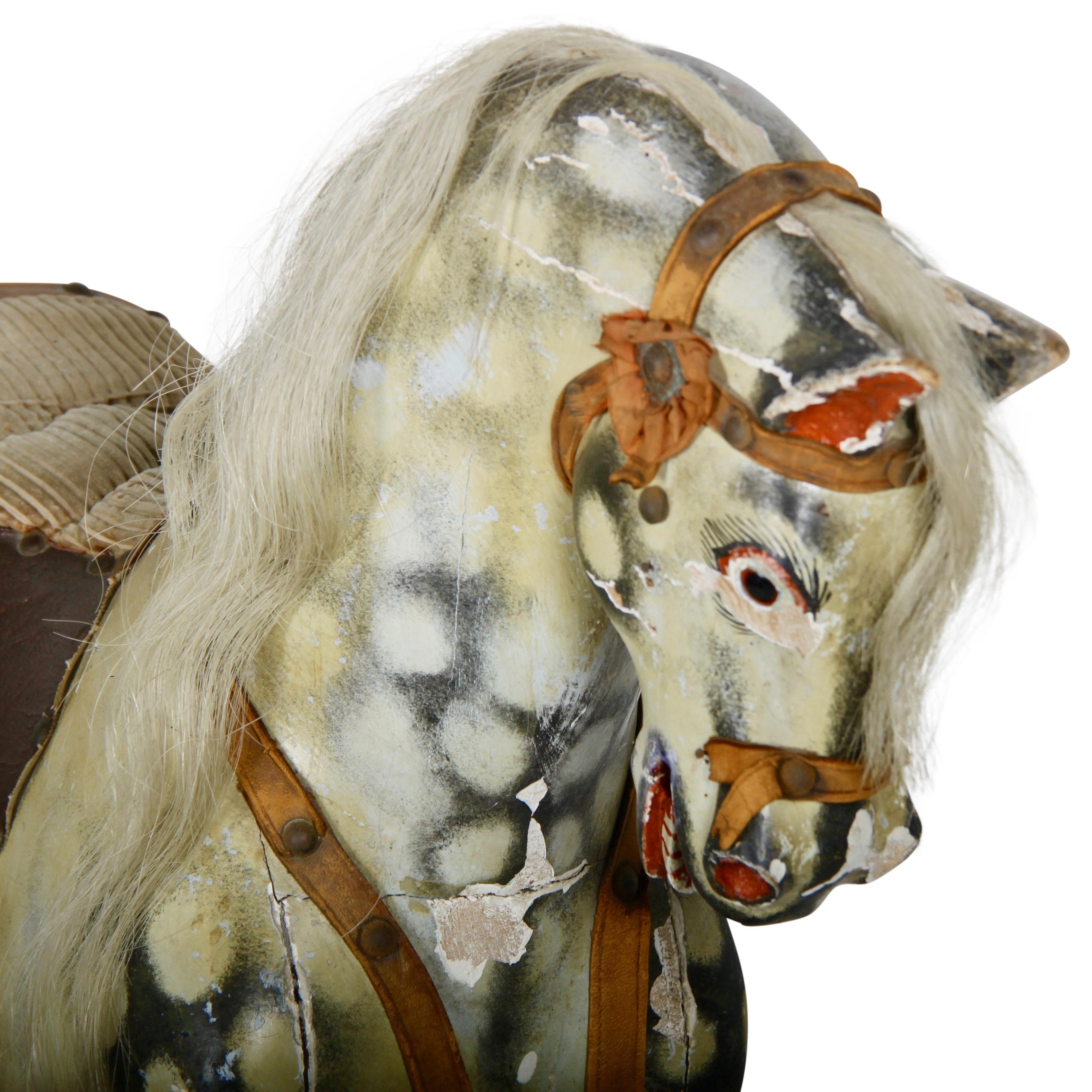 An early-20th century English carved and painted 'dapple grey' rocking horse with original fitted saddle and stirrups, and horse hair mane and tail.
Wear and losses commensurate with age / use.