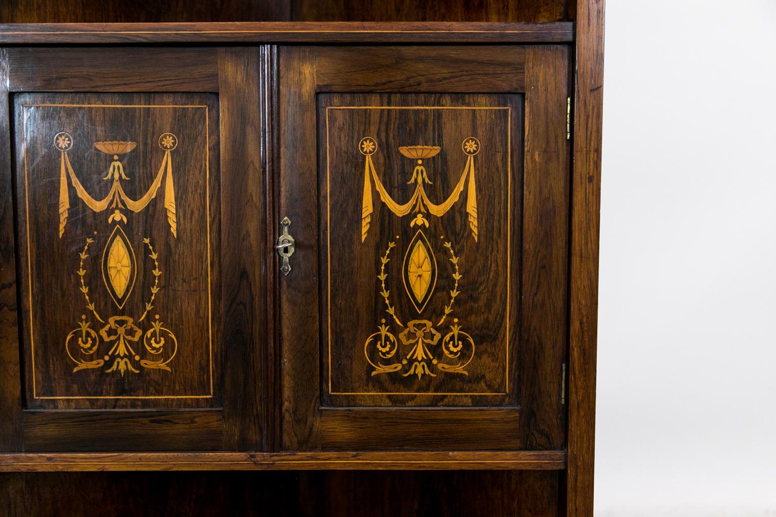 This English Edwardian rosewood corner cabinet is inlaid with fans, arabesques, and drapery swags. The upper section has opposing beveled glass mirrors with side panels with triple turned spindles, and all three top levels terminate in turned
