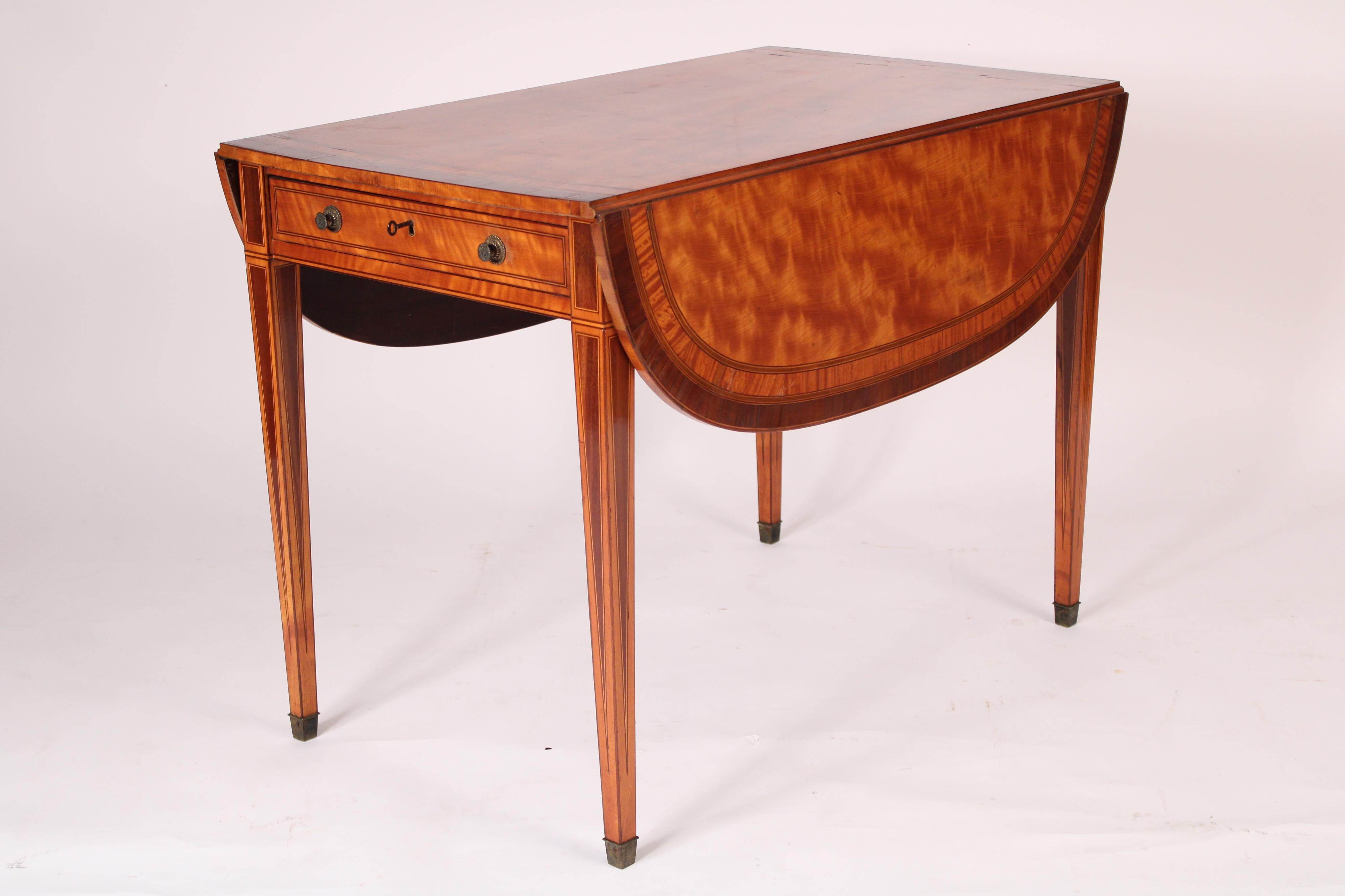 English Edwardian satinwood pembroke table, circa 1900. With a satinwood rectangular top with mahogany crossbanding and stringing, 2 D shaped drop leaves, a frieze drawer with two brass knobs, resting on square tapered satinwood legs with mahogany