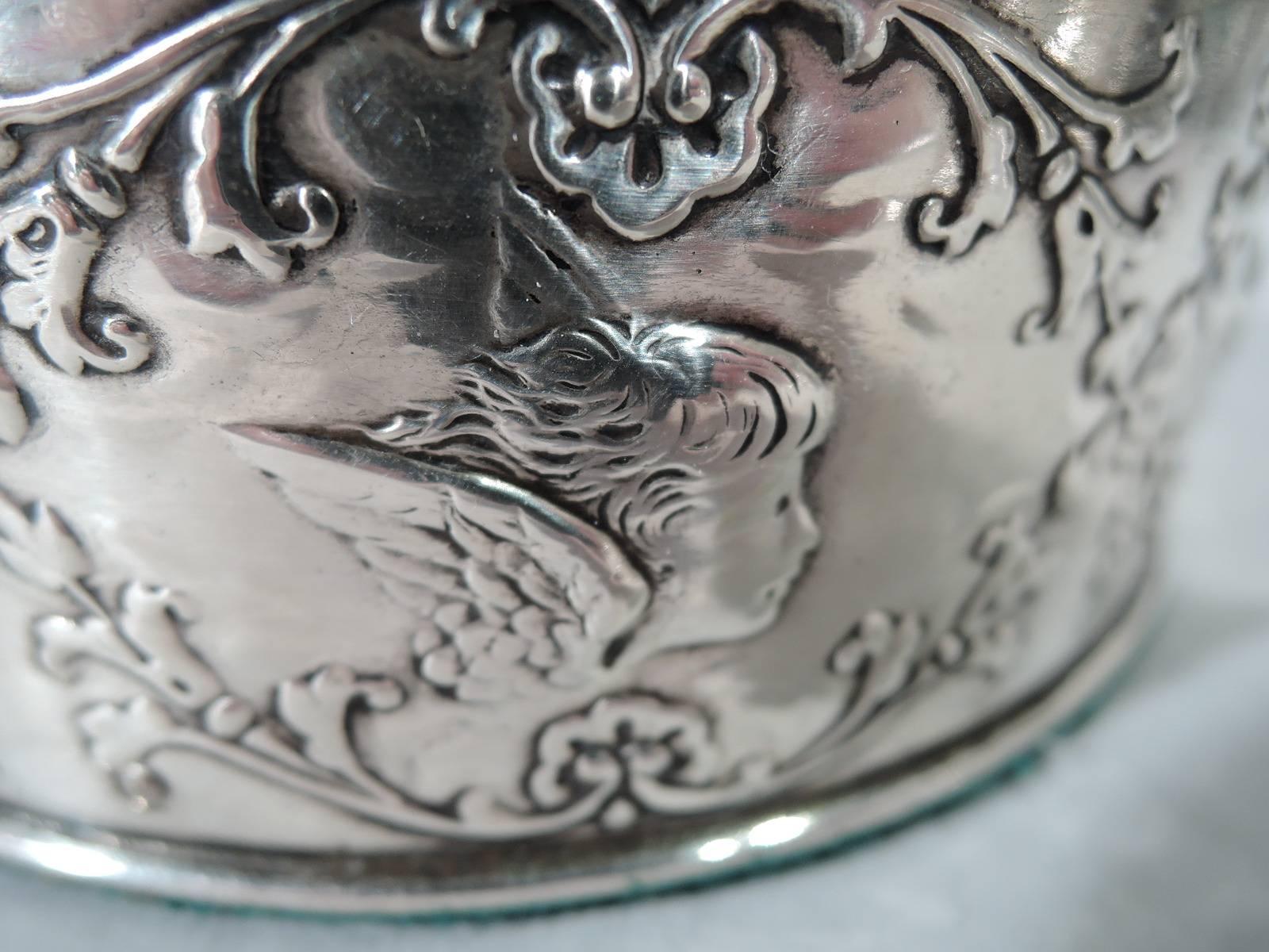 Edwardian sterling silver wine bottle coaster. Made by William Comyns in London in 1903. Straight sides and molded rims. Encircled with floral garland inset with winged cherub heads. Stained-wood well has central silver frame with engraved armorial.