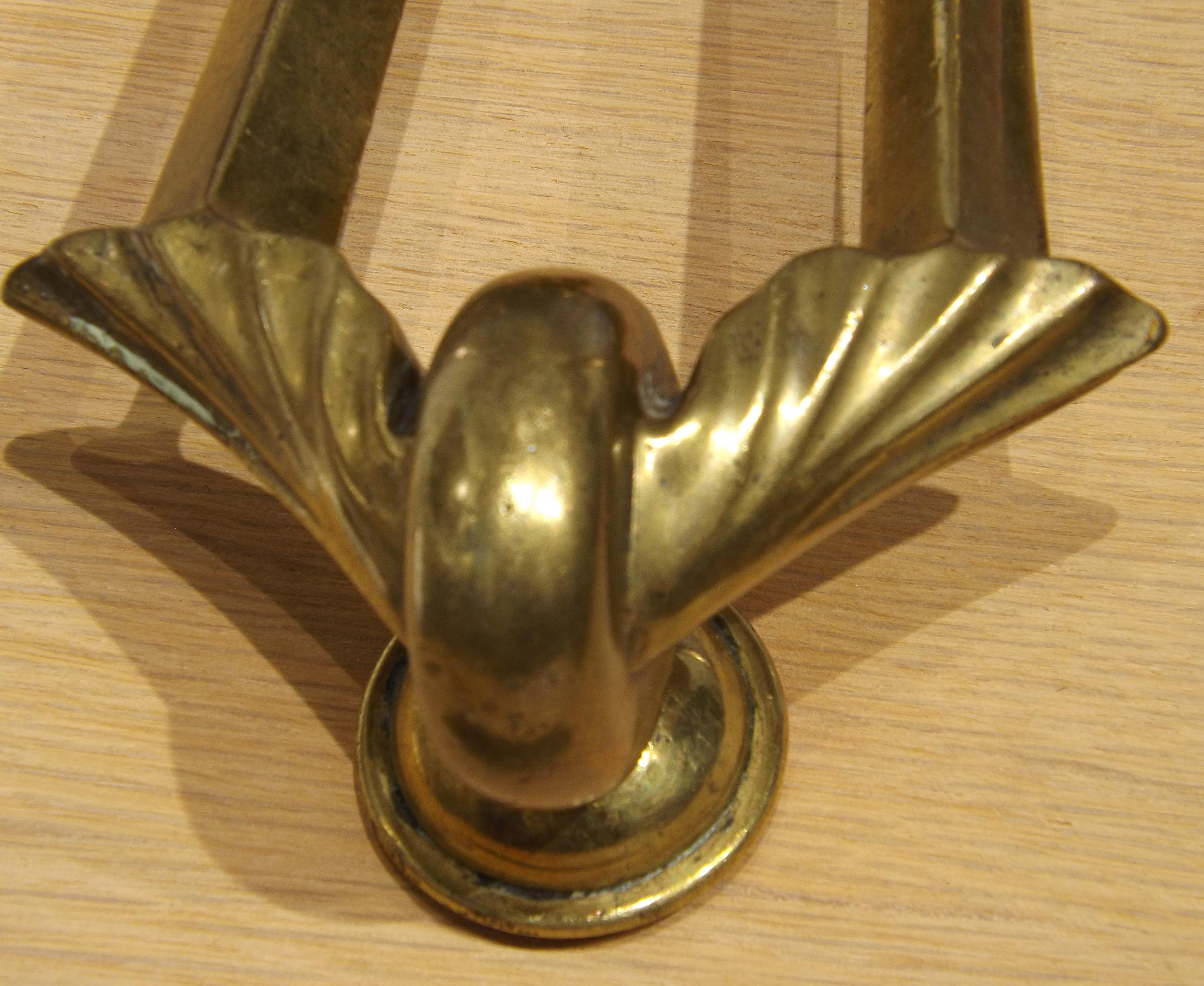 A magnificent brass door knocker in the shape of a winged wheel, from circa 1900. Designed to be mounted to a door, and complete with matching brass strike plate. Temporarily mounted to a wooden board for display purposes. When mounted on a door the