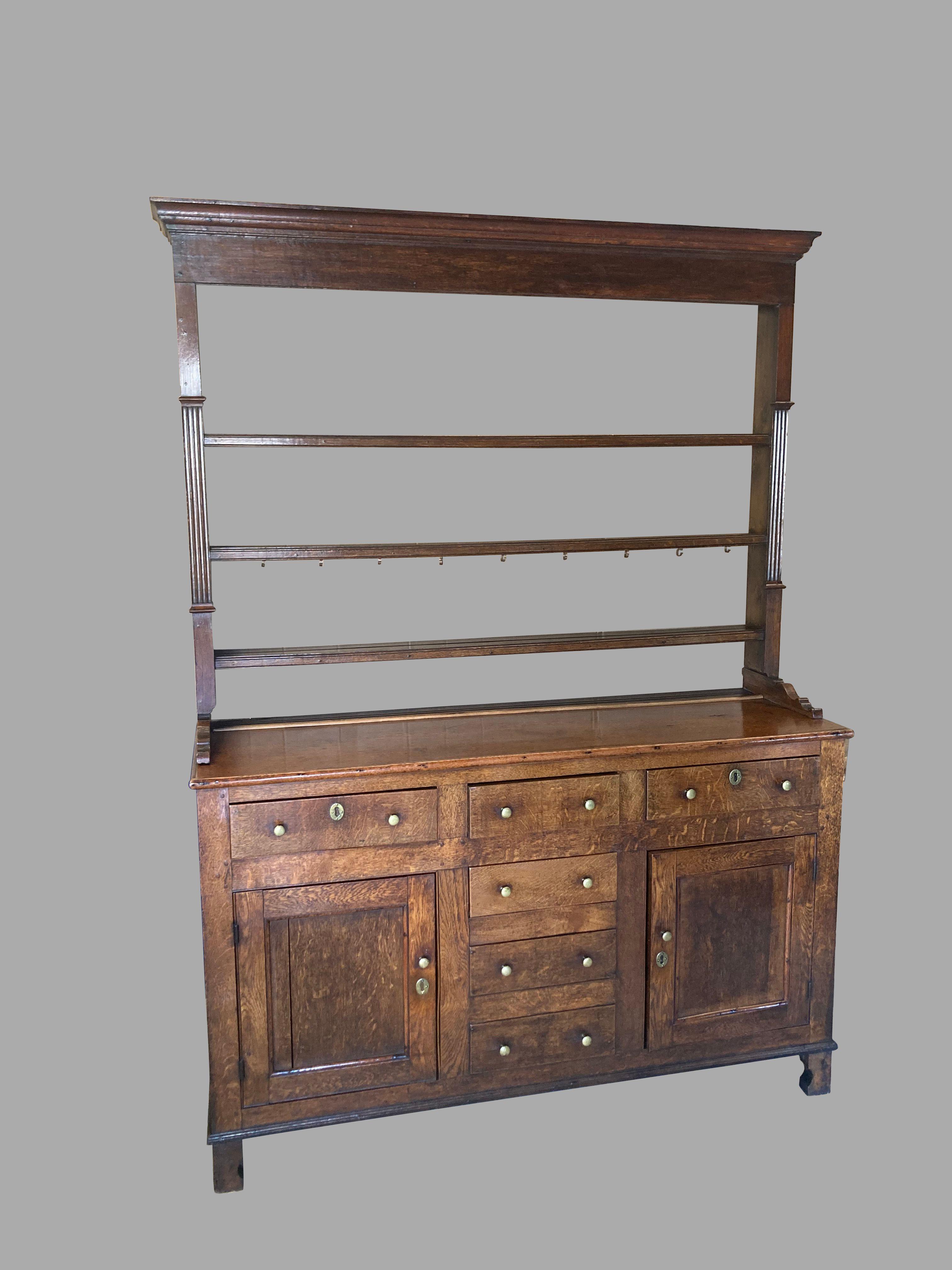 A good English solid oak high dresser, often called a Welsh dresser, in 2 parts, the upper stage with an open back, the 3 shelves mortised into the sides, retaining some hooks for cups. The sides are reeded and terminate in a well-designed scalloped