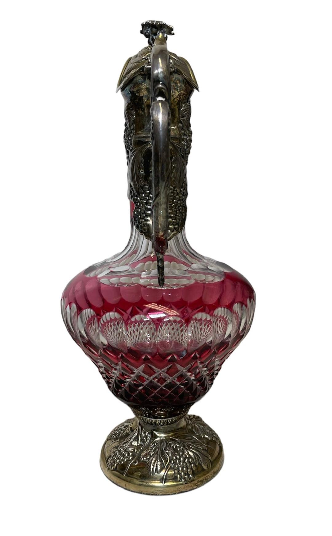 This is an English Electroplated Silver and Cut Crystal Claret, Wine Jug or Decanter. It depicts a red and clear crystal body adorned with a pattern of oval figures and a cluster of diamonds. The crystal body is mounted in electroplated silver at