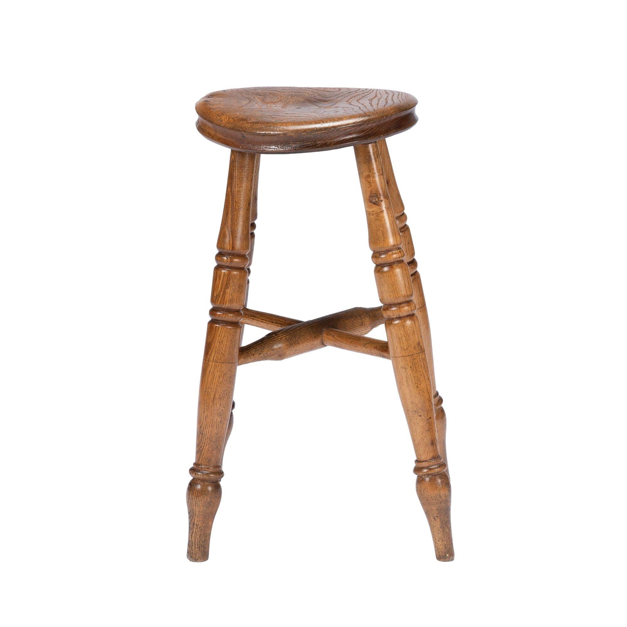 English elm wood circular seat milking stool on turned legs terminating in tulip bulb feet. Joined by ‘X’ stretchers. 
England, circa 1860.