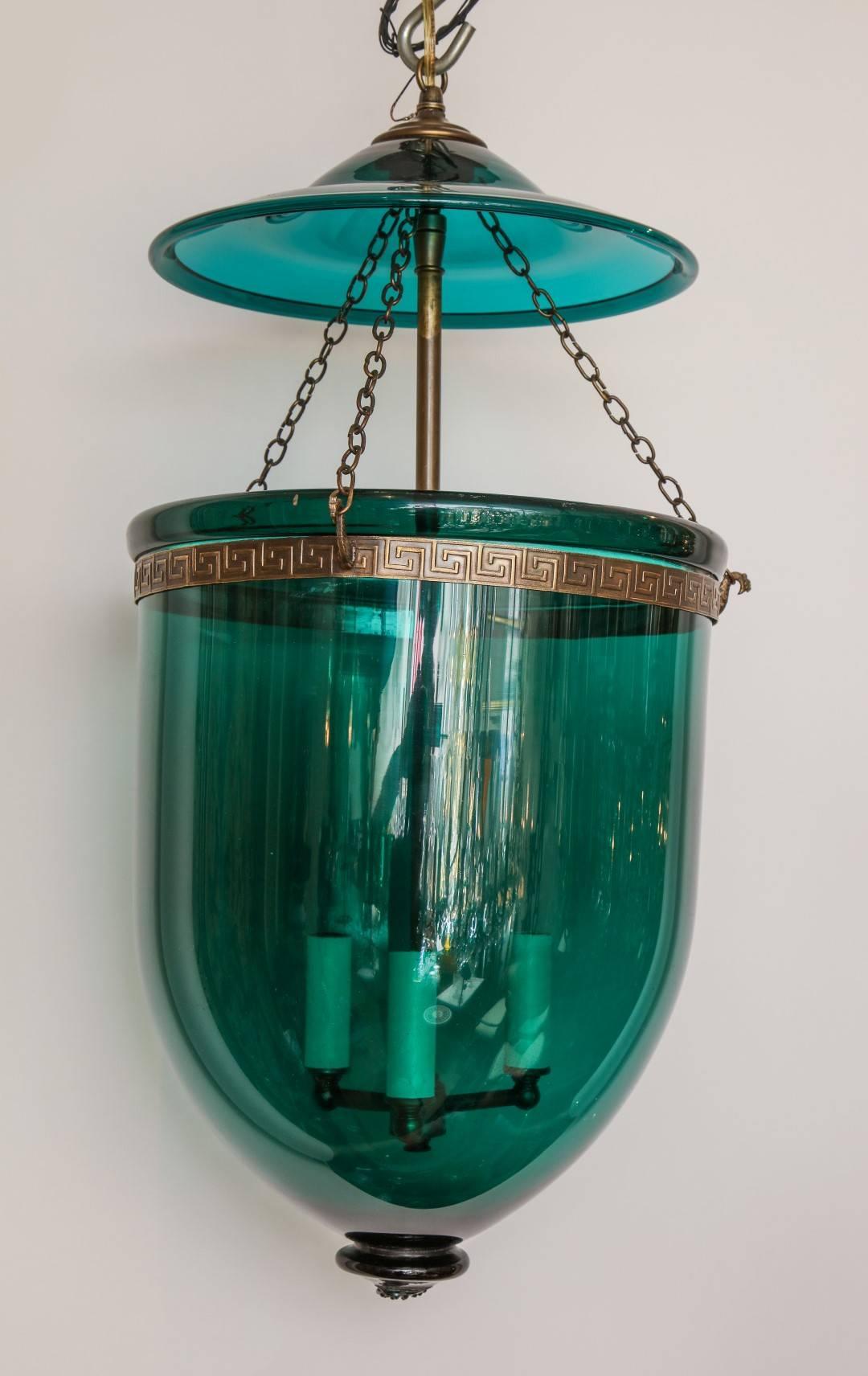 An English green hanging glass lantern, suspending a tripartite candelabrum with etched Greek key motif at collar, original smoke bell and brass fittings. New, standard wiring. Includes ceiling canopy and chain with matching antique brass