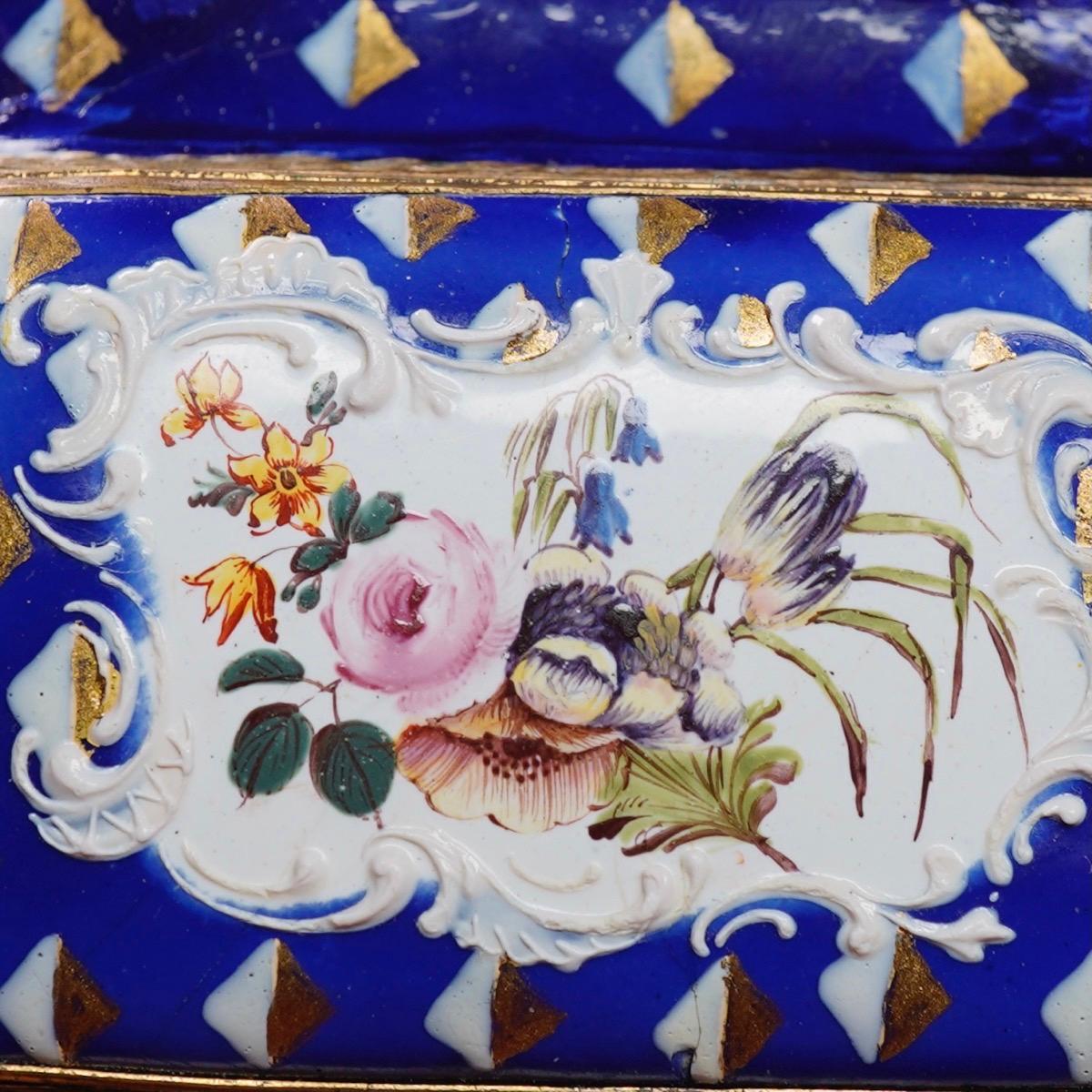 English enamel box of rectangular form, painted with white/gilt squares on a deep sapphire blue ground, the center with a panel of flowers set within a white Rococo scroll panel,
circa 1780.