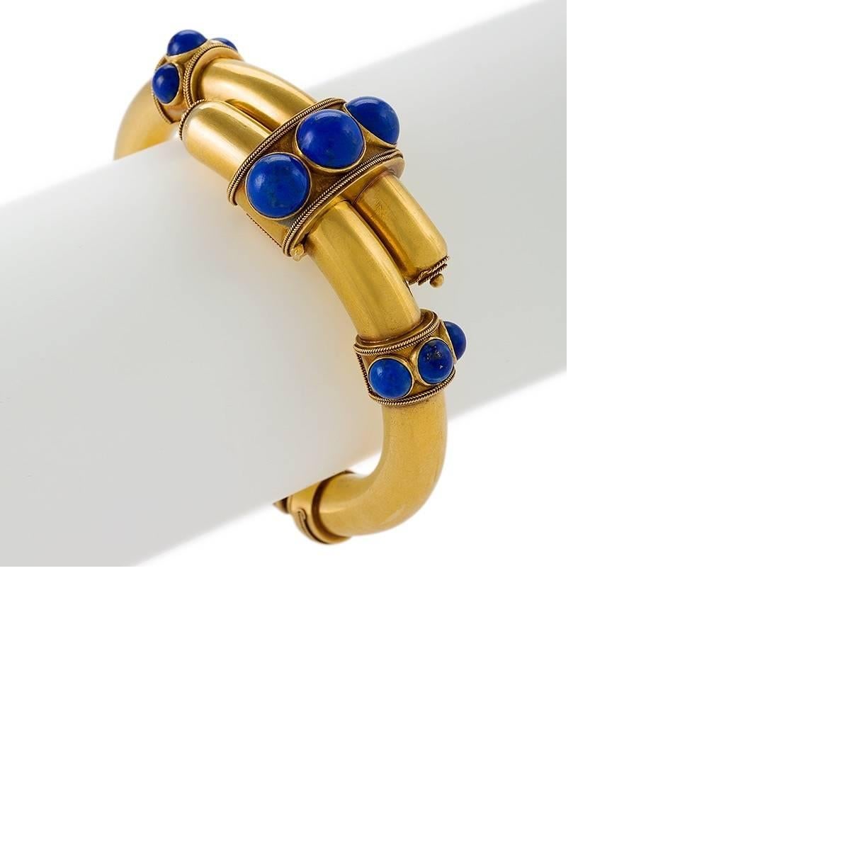 An English Etruscan Revival 18 karat gold and 14 karat gold spring back bracelet with lapis lazuli.  The hinged bracelet is set with 9 cabochon bezel set lapis lazuli stones.  The bracelet is designed in an Etruscan Revival cross over motif