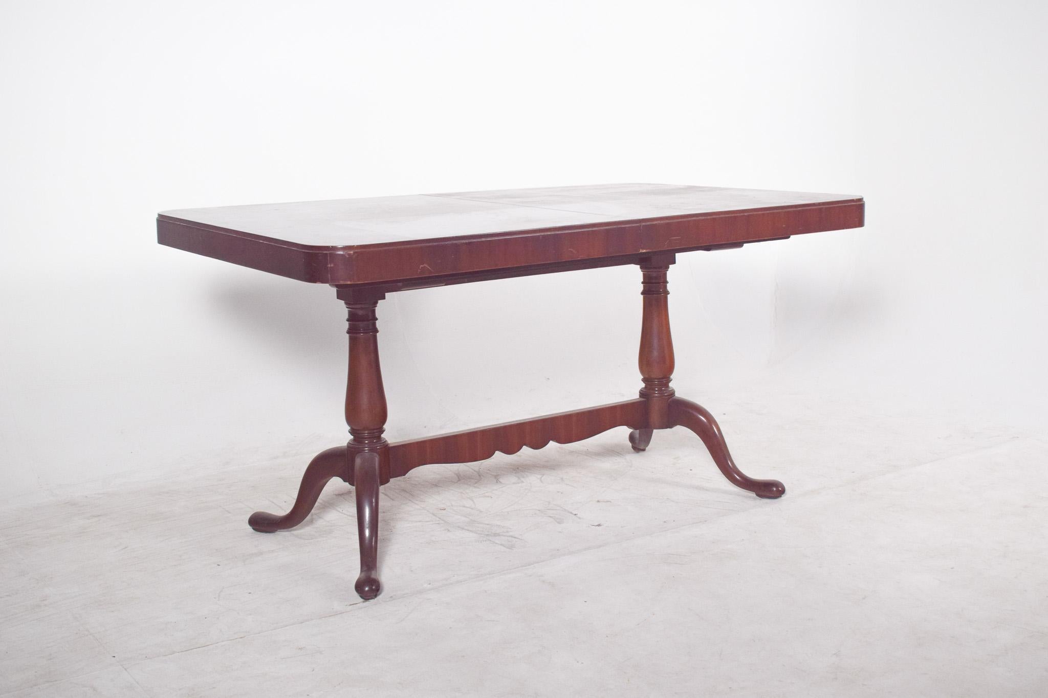 Extendable dining table in walnut and walnut root. Rectangular in shape, with rounded corners, resting on two turned centre legs connected by a cut-out crosspiece. Each foot ends in three curved cabriole supports, giving the whole a light and