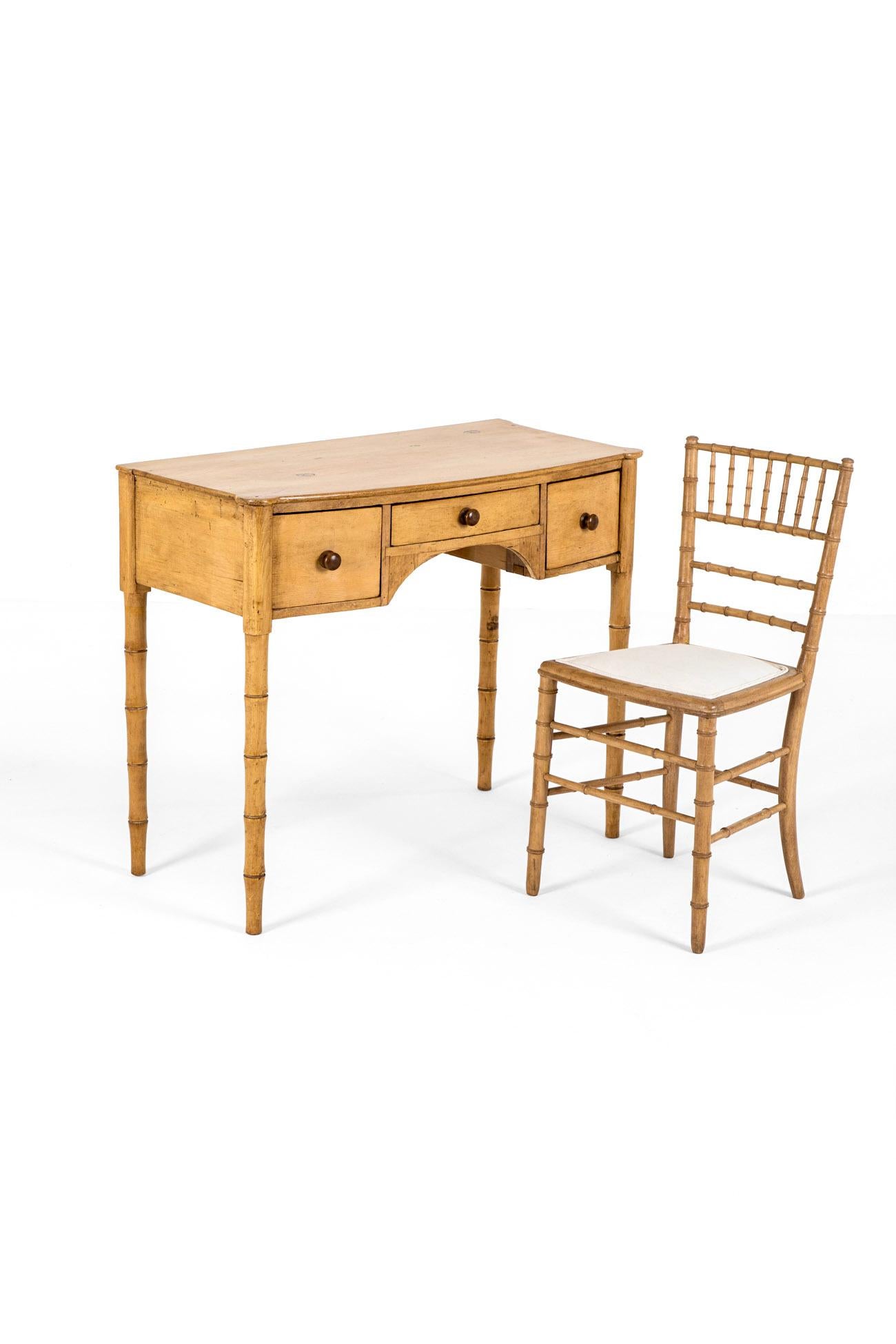 Un'incantevole toeletta e sedia in pino finto bambù con fronte ad arco, in buone condizioni.

Il tavolo ha un piano sagomato che sovrasta una configurazione di due cassetti profondi e uno centrale con fregio.

Il tutto poggia su quattro gambe di