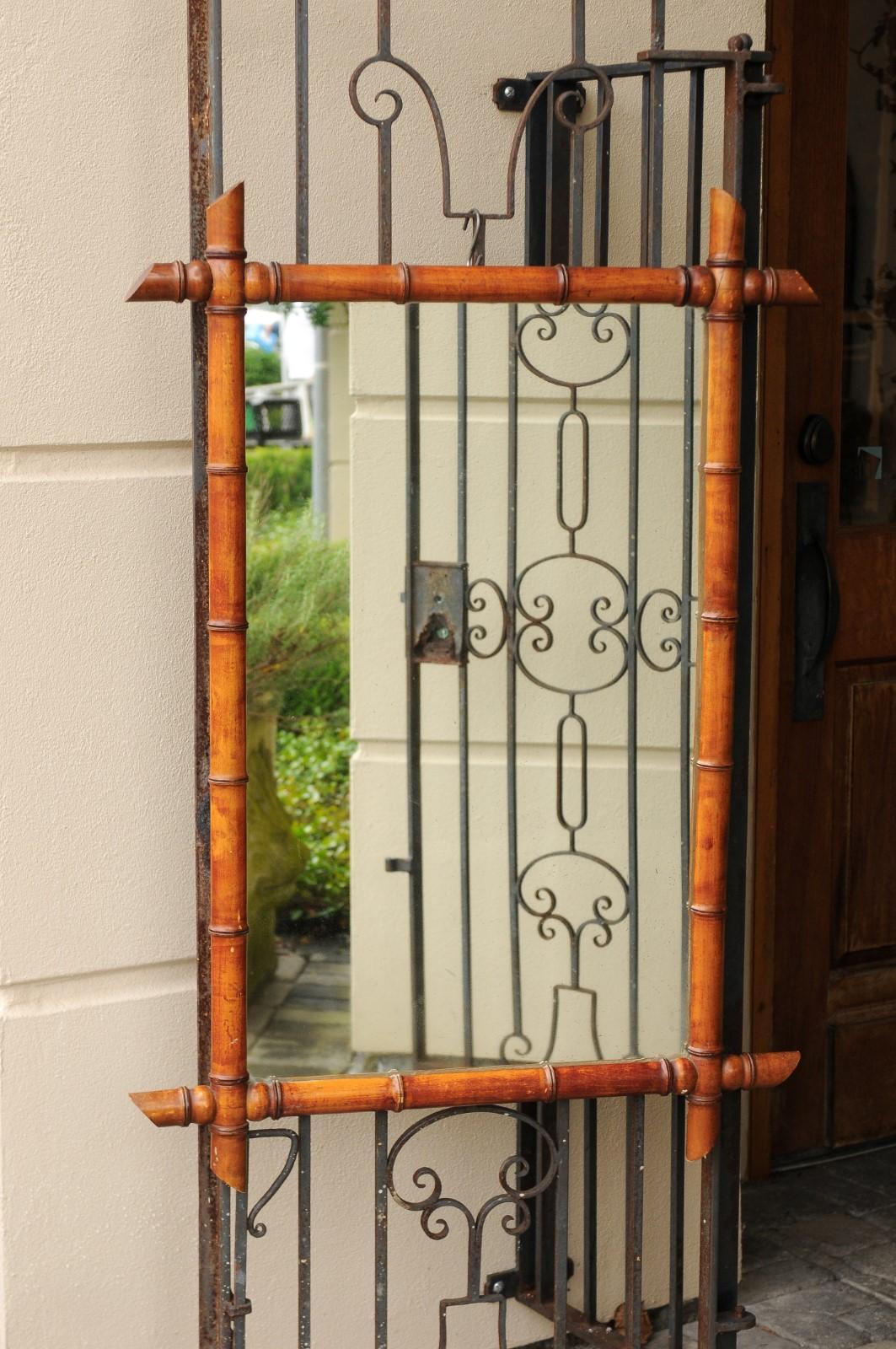An English faux-bamboo mirror from the early 20th century with clear mirror. Born during the vibrant Roaring Twenties, this English faux-bamboo mirror features a linear silhouette, adorned with four simple intersecting faux-bamboo staffs, securing a