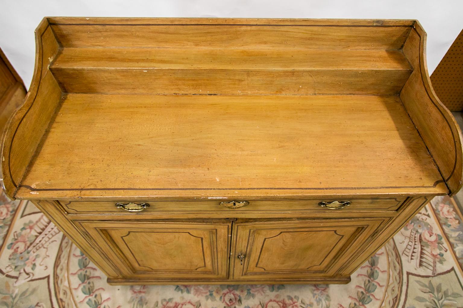 The top of this server has a four-inch plateau shelf supporting a three-sided shaped gallery. The top and front are painted with simulated brown inlay. The lower doors have a working lock and key. The brasses are later.