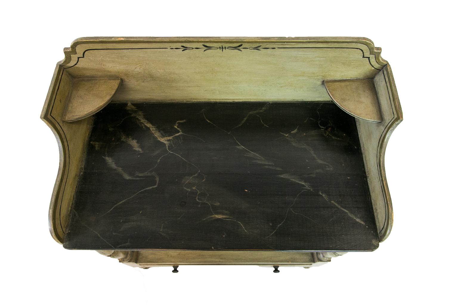 The top surface of this English faux painted washstand is painted to simulate marble. There are highlights in darker green bands on the edges and drawer fronts with black lines connecting stylized opposing bell flowers on the backsplash and drawer