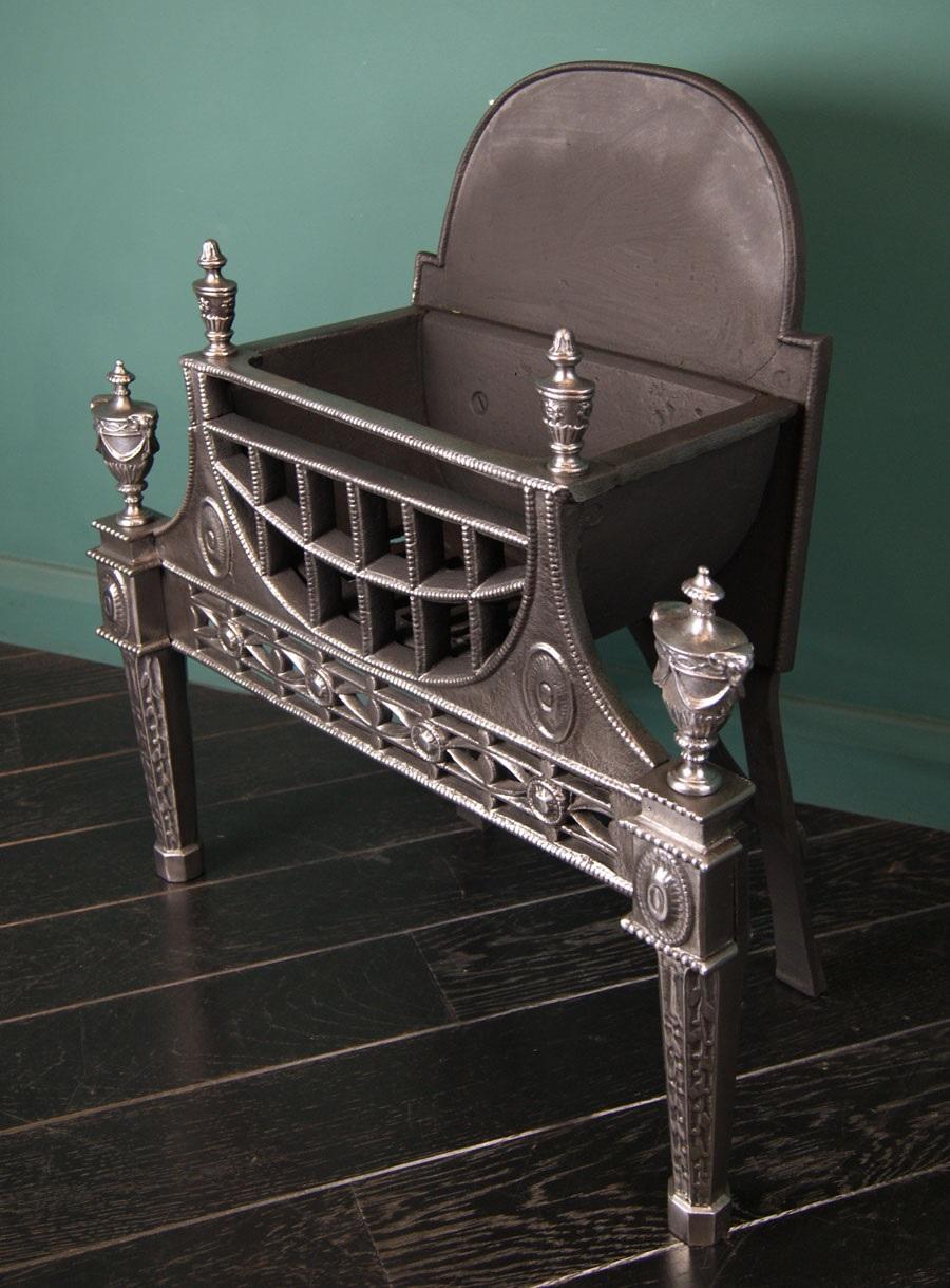 An English cast-iron fire grate in the manner of Robert Adam. The openwork fret with roundels set between decorative legs and urn finials with swag and rams head detail uppermost. Beaded edge throughout with a curved fire grill. 
Small crack to