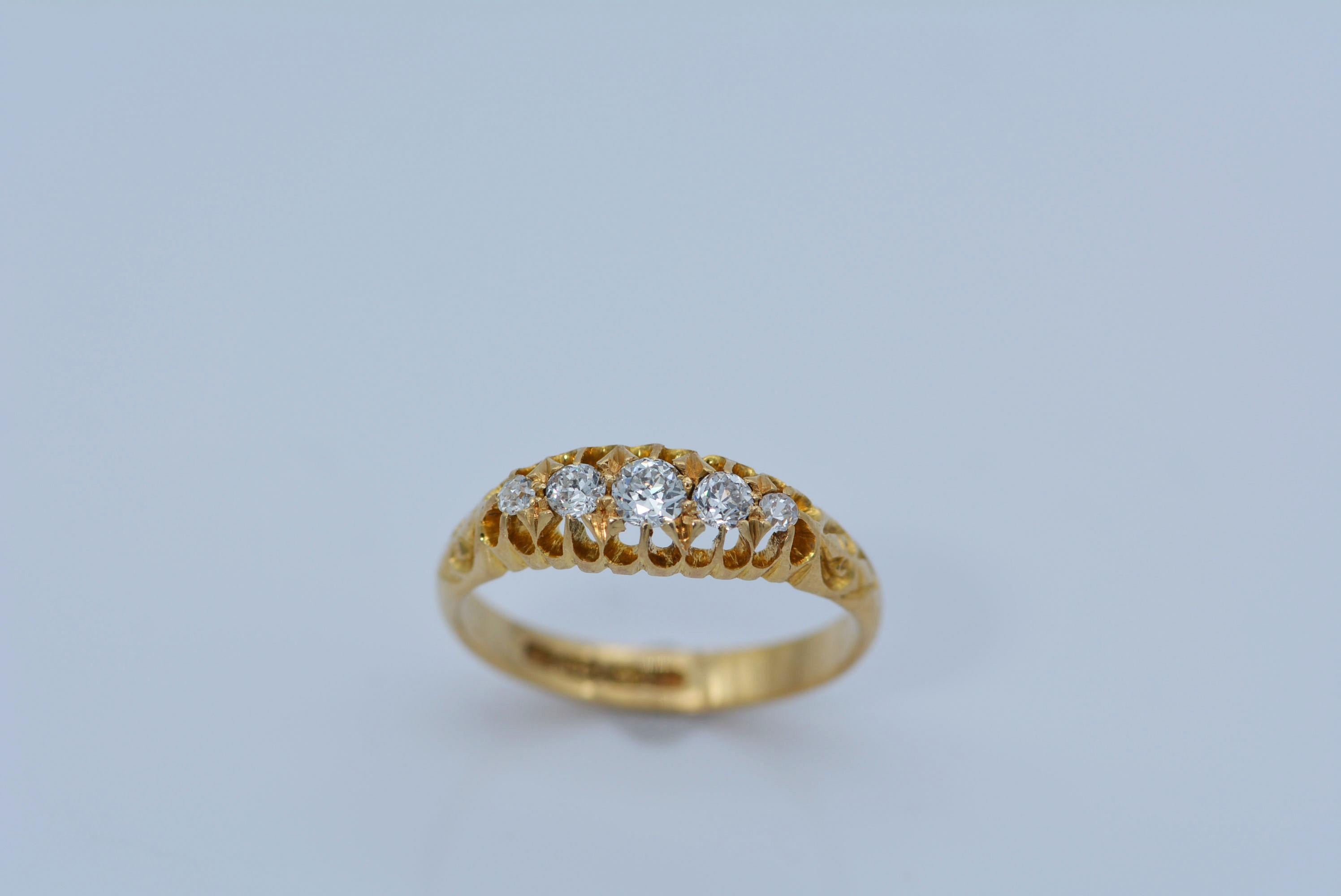 This buttery yellow gold ring of english origin contains five antique diamonds that are graduating in size. 
The largest diamond is set in the center of the ring.

The handmade band is 18 karat yellow gold and has beautiful carved prongs acting as