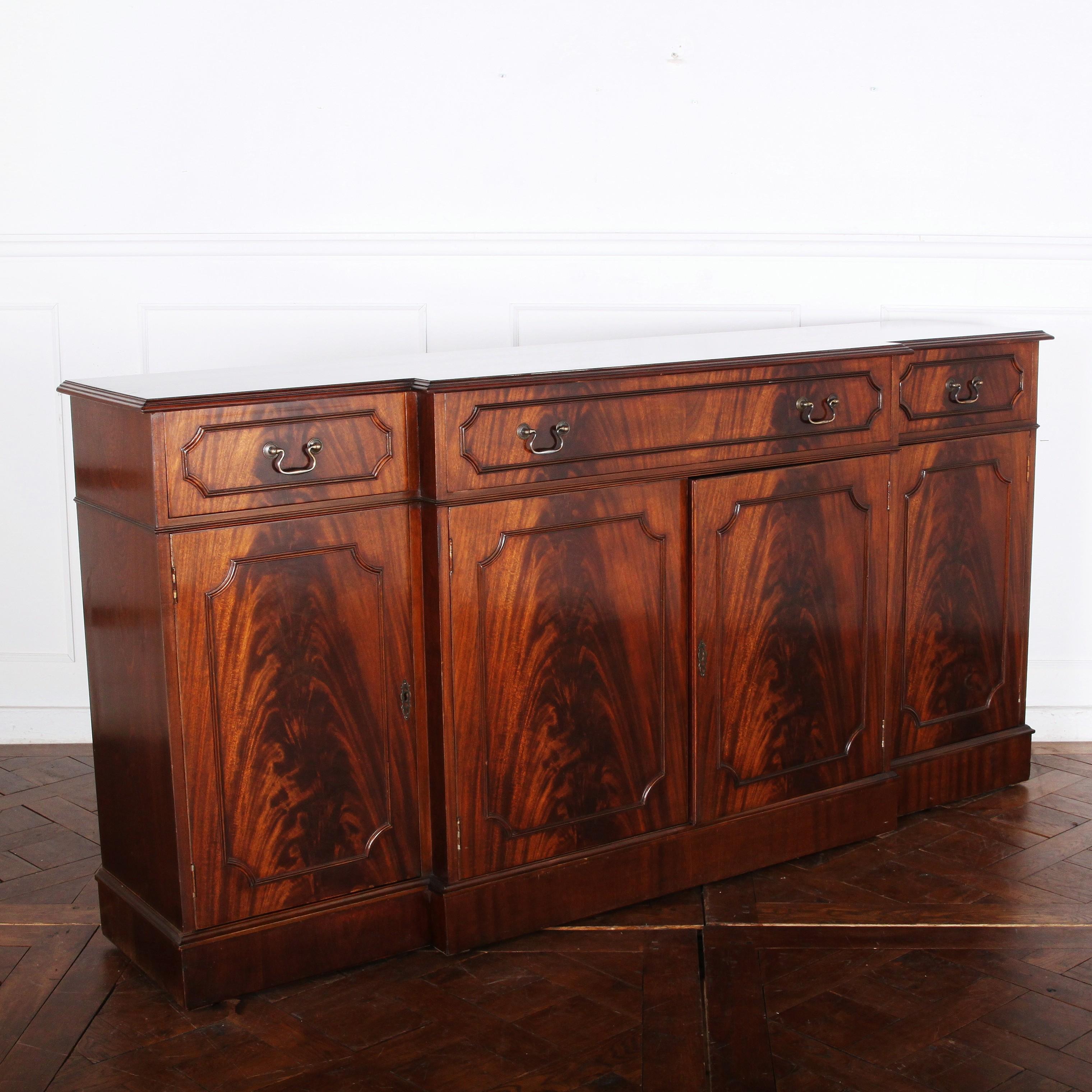 An English break front mahogany side cabinet, the four doors with moulded details and flame mahogany fronts and with three upper drawers. Adjustable shelves in the lower cabinets. The relatively shallow depth makes this a useful storage option in