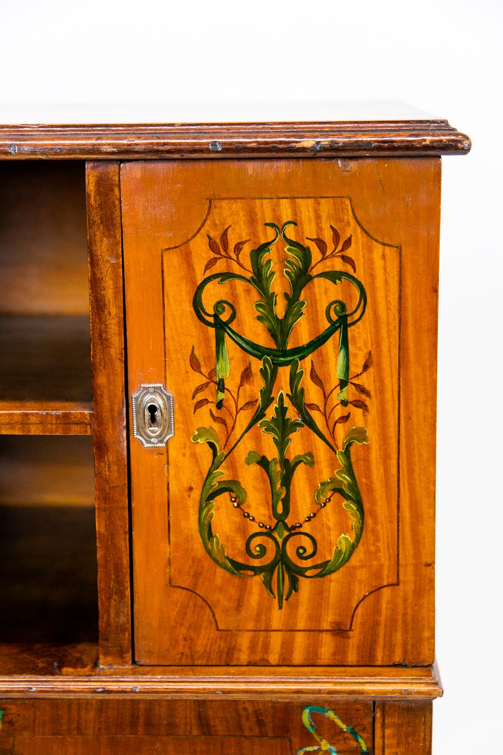English floral painted satinwood cabinet with two cubby holes, four doors, and two drawers. It has lovely painted ribbon and floral swag motifs; the doors with quarter corner inlaid panels.
  