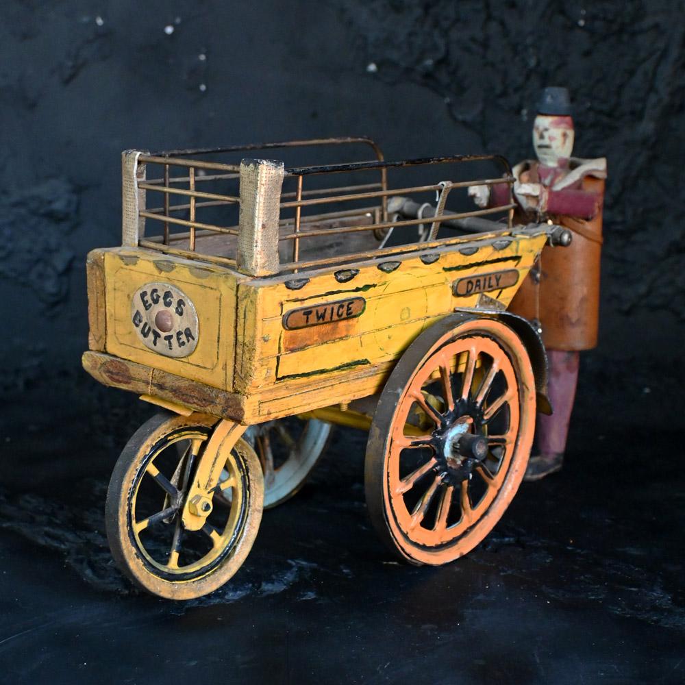 English folk art shop counter milk man figure. 
A charming mid-20th century folk art shop countertop display figure. In the form of a man pushing a milk cart. Completely scratch built from wood, leather, and metal. this item may have sat on a