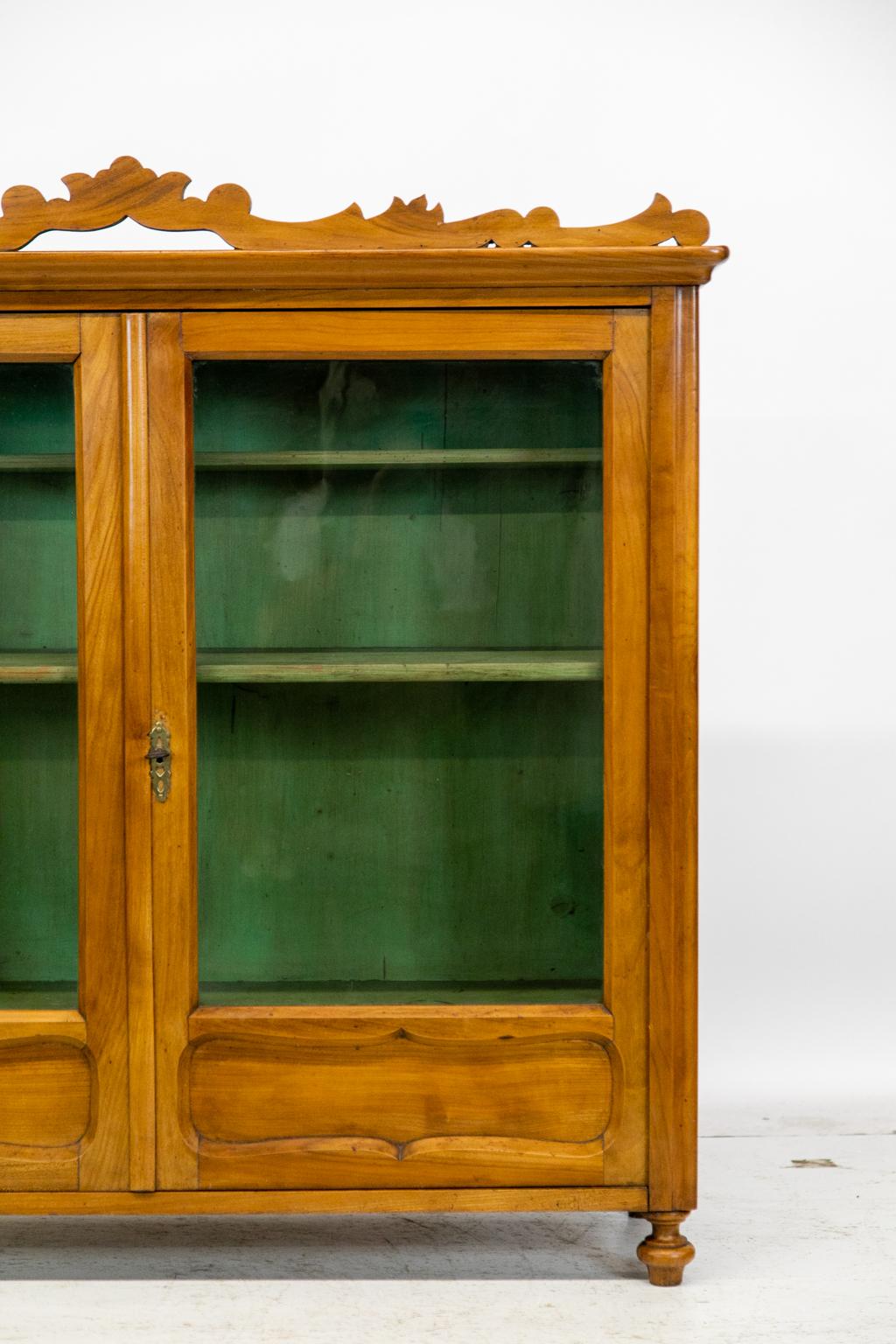 English fruitwood cupboard/cabinet has an applied carved crest. The doors have shaped molded lower panels that hide two interior drawers. The interior has the original green paint. The doors have old wavy glass panes framed with beveled interior