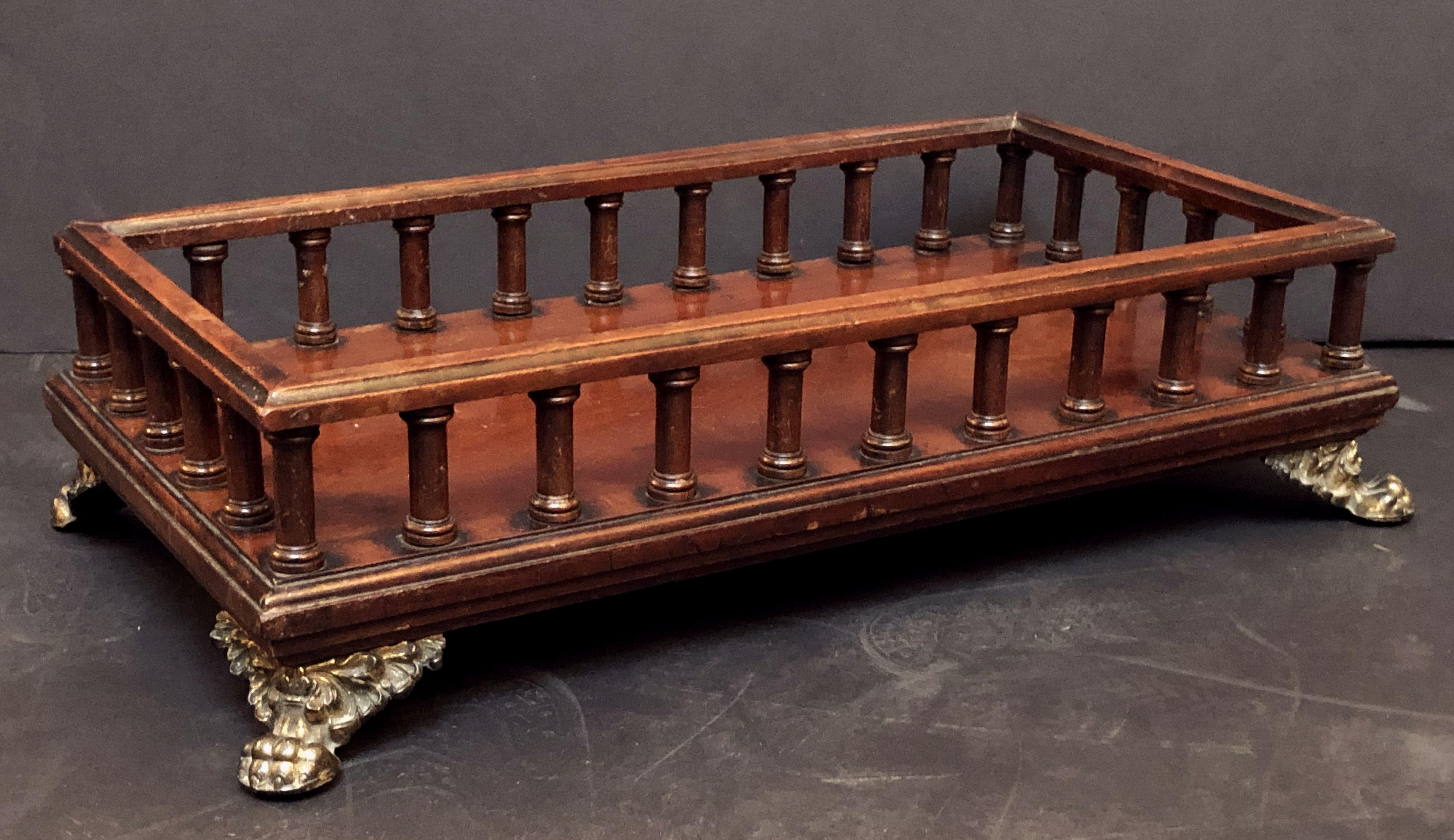 A fine English footed rectangular gallery tray or book stand of mahogany for the library from the Regency period, featuring a turned column gallery on a molded base with hairy claw feet of brass at each corner. Underside with marbleized paper