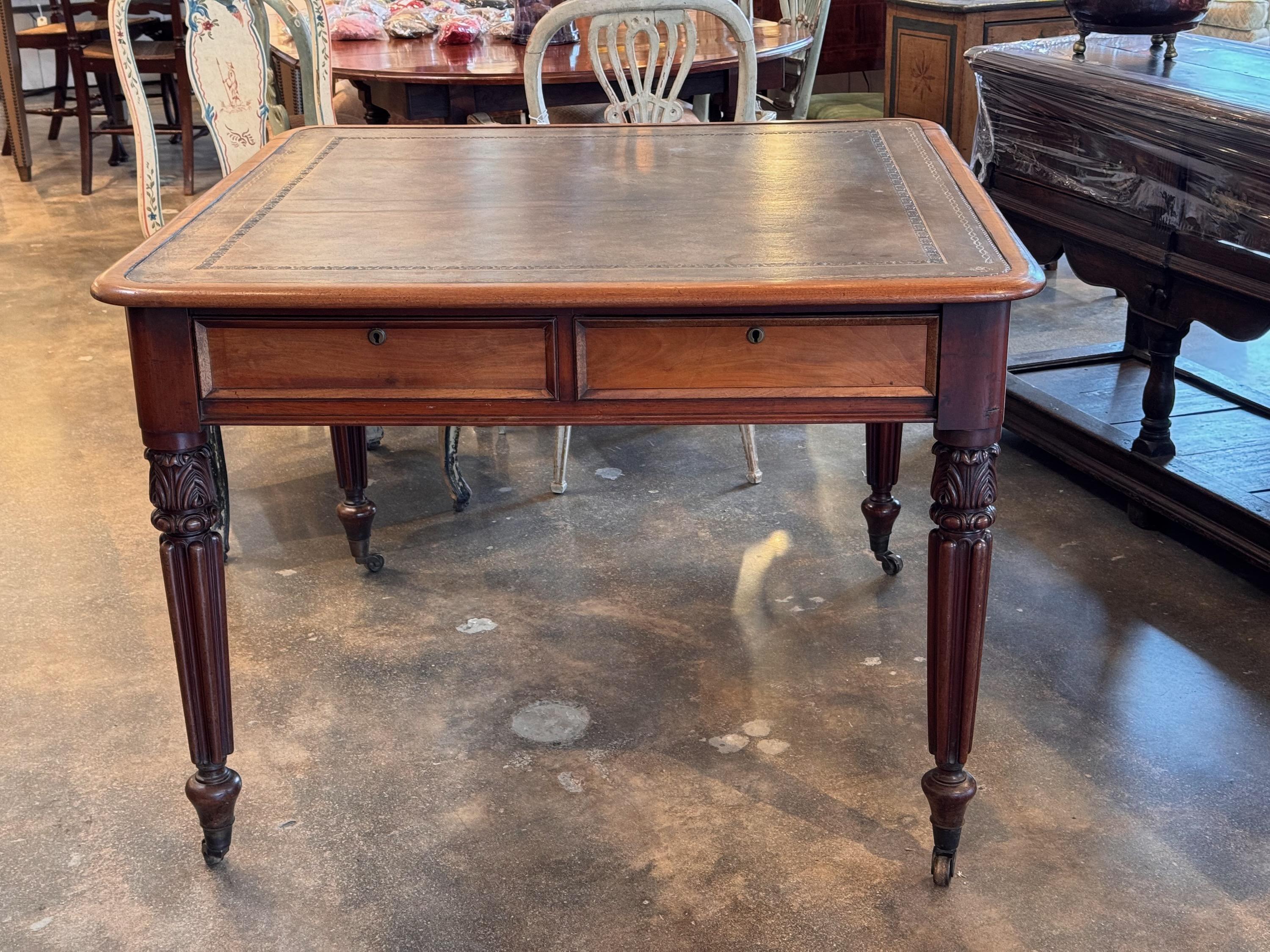 This elegant 19th-century English game table features a richly patinated leather top with intricate gold tooling. Four discreet drawers provide storage, while the beautifully carved, fluted legs rest on caster wheels for mobility. A versatile piece,