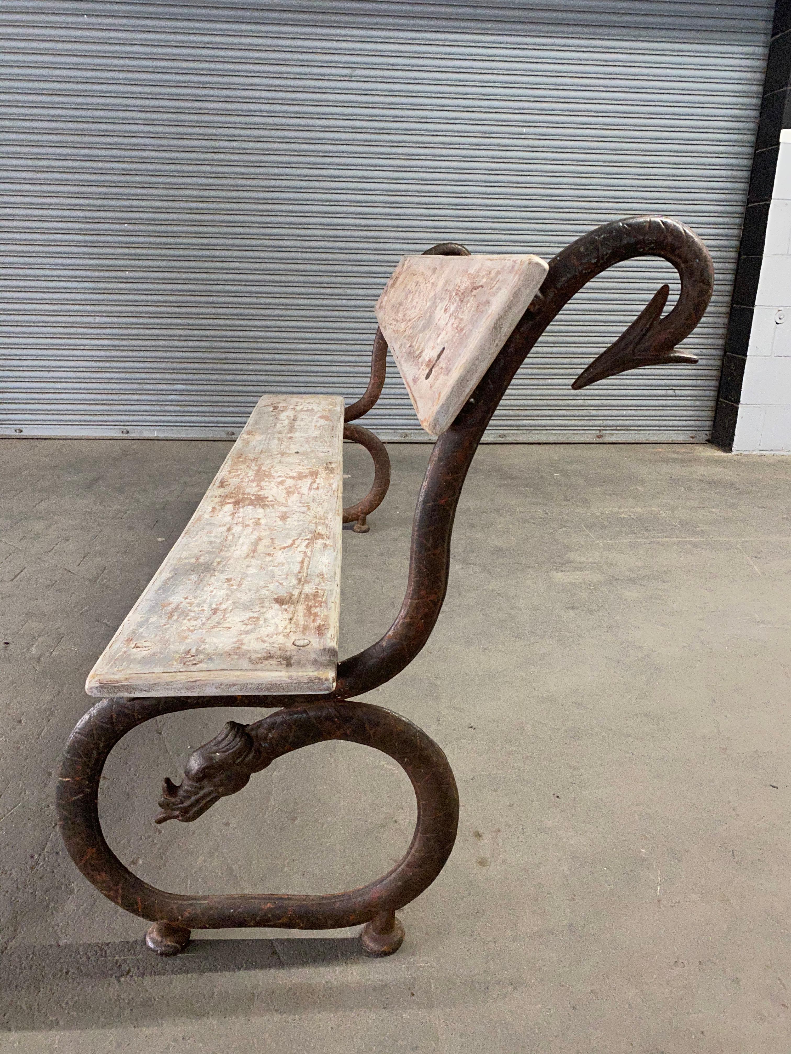 A sculptural English (or French) garden bench with the supporting cast iron base in the shape of stylized dragons or serpents, open to interpretation. The new wood planks that form the seat and back are new and have been finished in an antique
