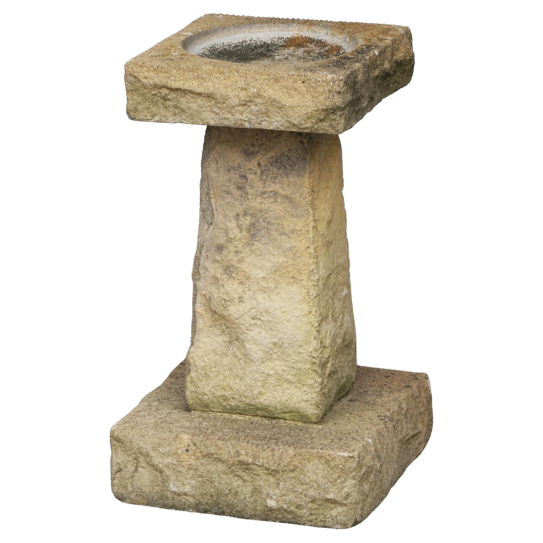 A fine English garden bird bath of cut hamstone, featuring a square top with round recessed bath area in the center, set upon a four-sided pedestal with square plinth base. The top and base with an etched radiating design.

Hamstone is the name