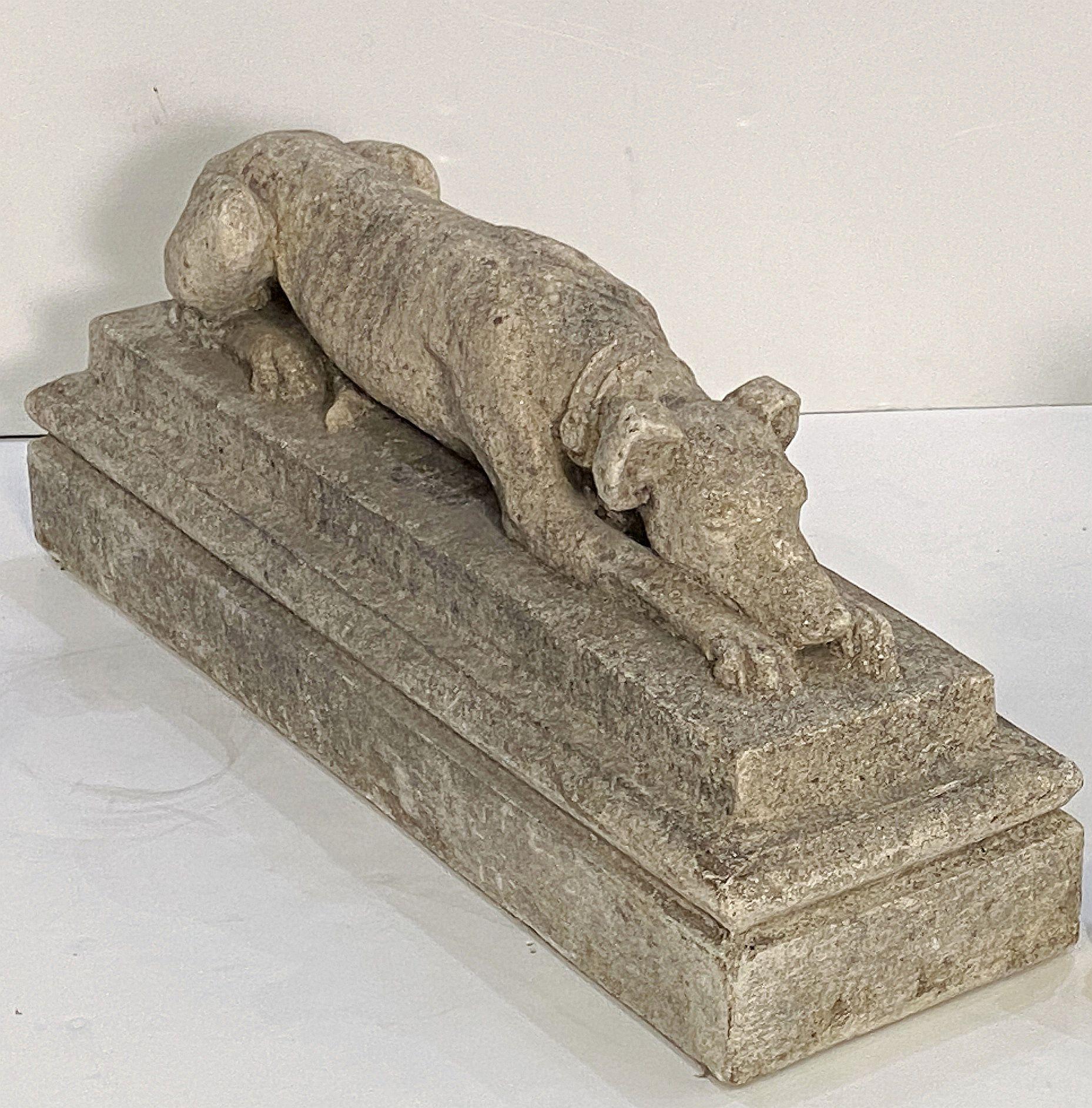 Chien whippet ou lévrier en pierre de jardin anglaise, finement modelé, en position couchée sur une longue plate-forme rectangulaire surélevée, avec un collier autour du cou.

Parfait pour un jardin ou une porte d'entrée.