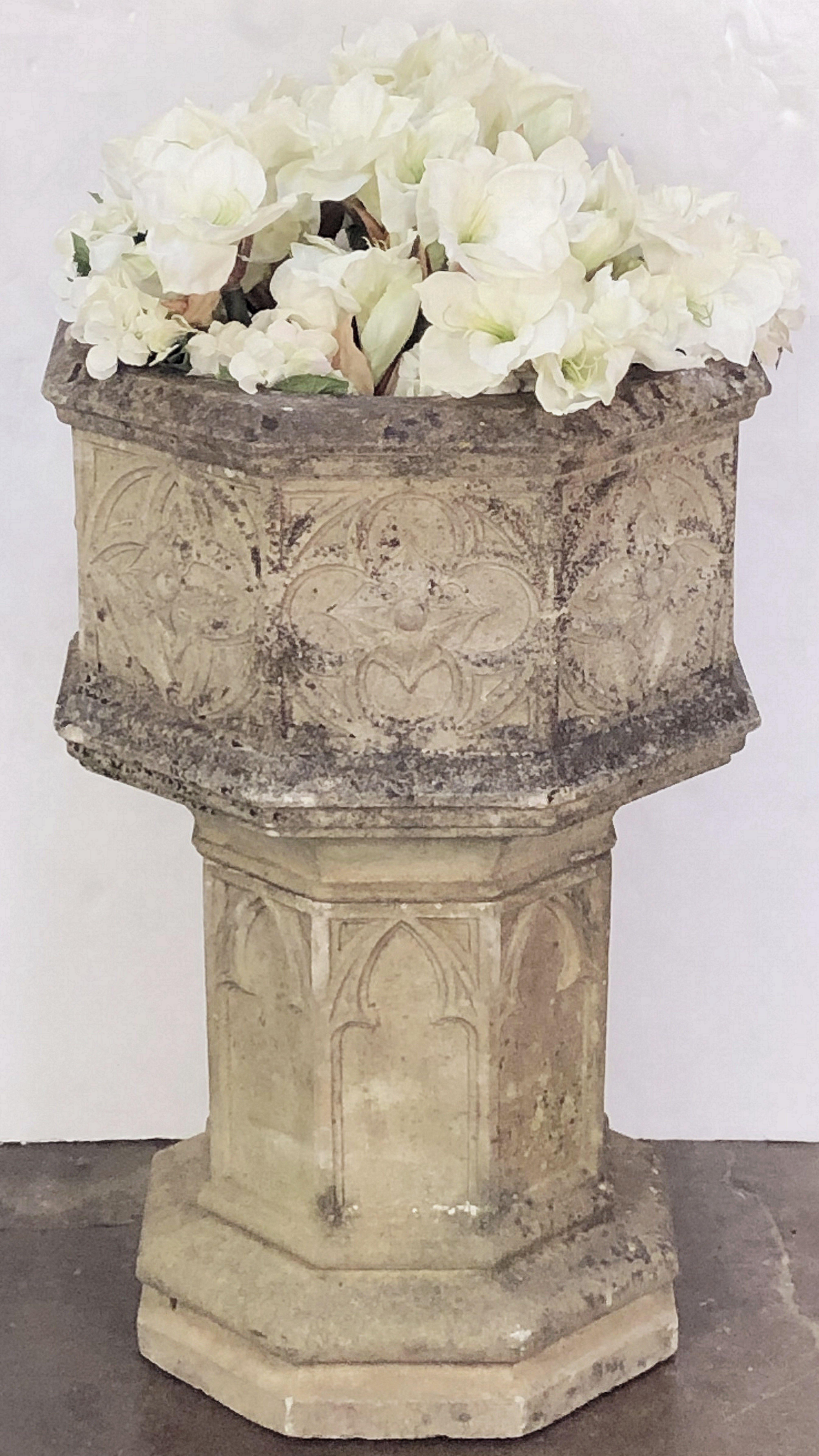 A fine English octagonal planter or garden urn of composition stone in the Gothic style, featuring a large eight-sided pot for planting with a decorative quatrefoil design around the circumference, set upon a fitted eight-sided pedestal column base