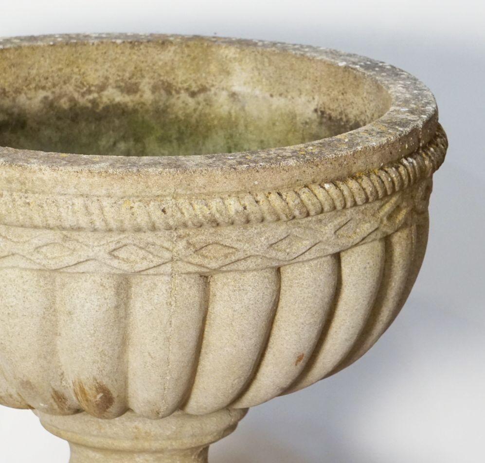 A handsome English circular garden stone urn (or planter pot) on a raised column plinth. 
The round urn featuring a lattice design around the top circumference and a fluted bowl. 
Resting on a round plinth featuring a Neo-Classical relief around