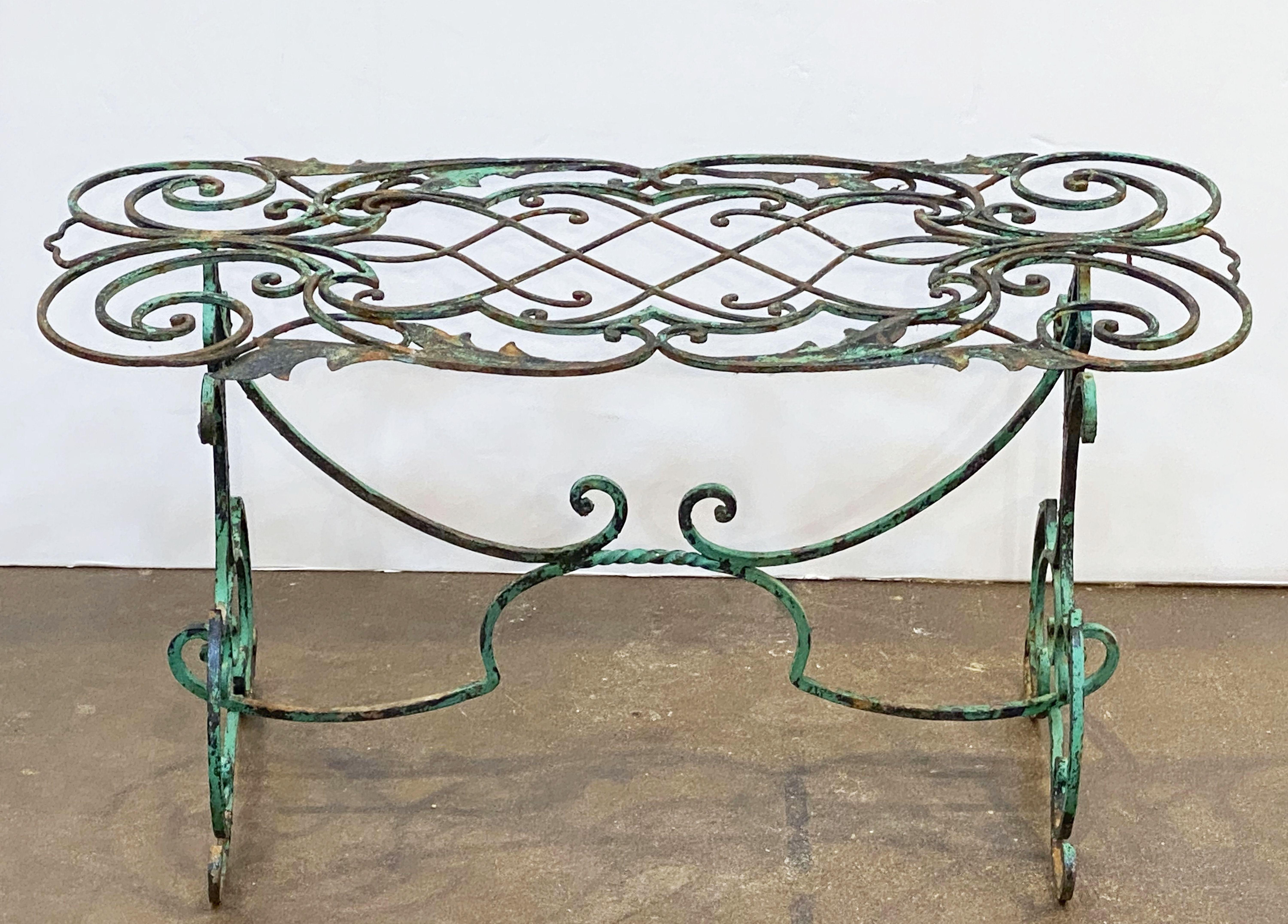 A fine English garden table of wrought iron with a verdigris painted finish, featuring a rectangular top on a stylish support of two legs and a stretcher, the whole with a fanciful pattern.