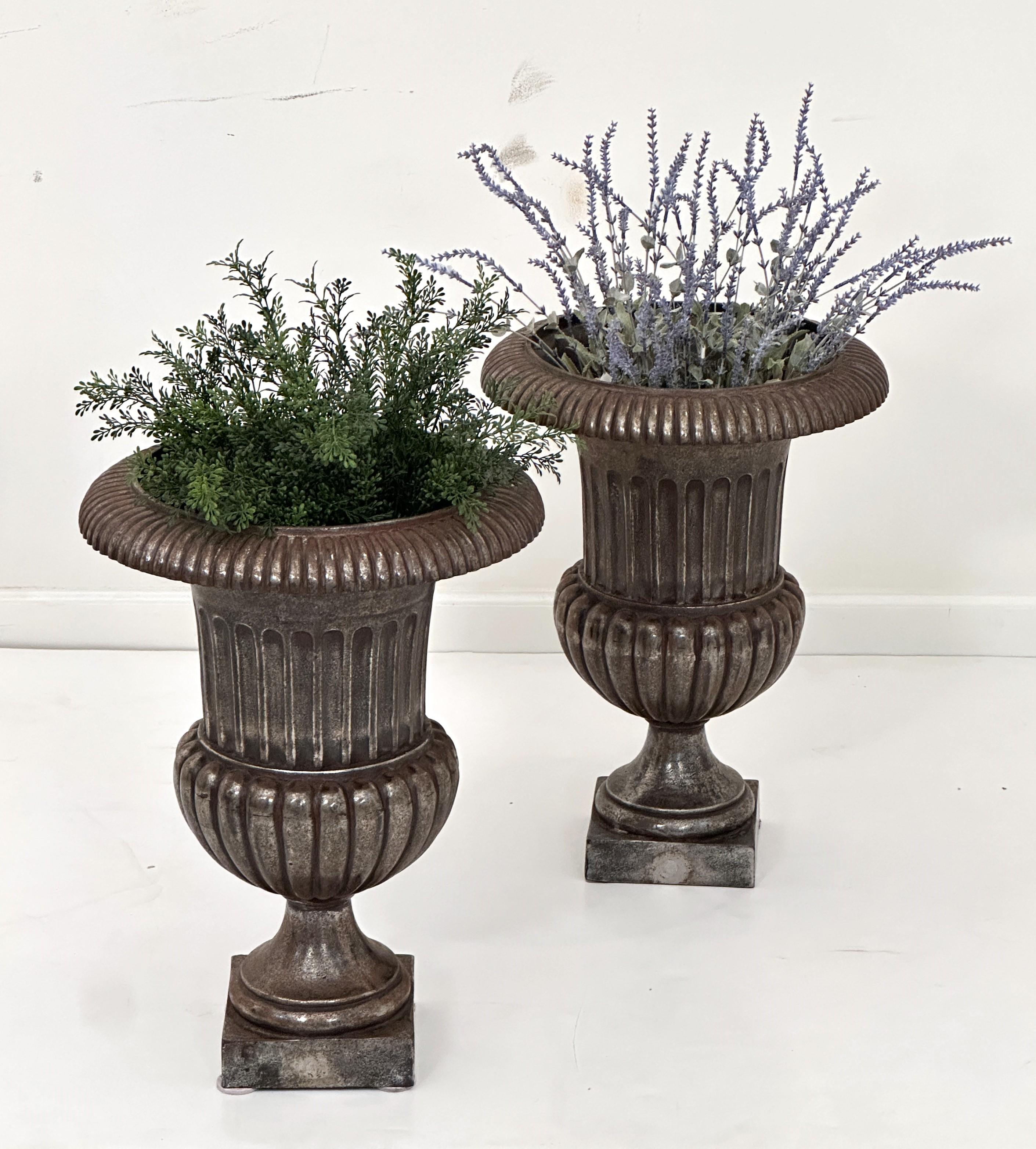 A fine pair of English garden urns or planter pots of burnished cast iron in the Classical or Medici style - each planter urn featuring a campana or bell shape with flared top edge over a fluted body, resting on a square plinth base.

Perfect for an