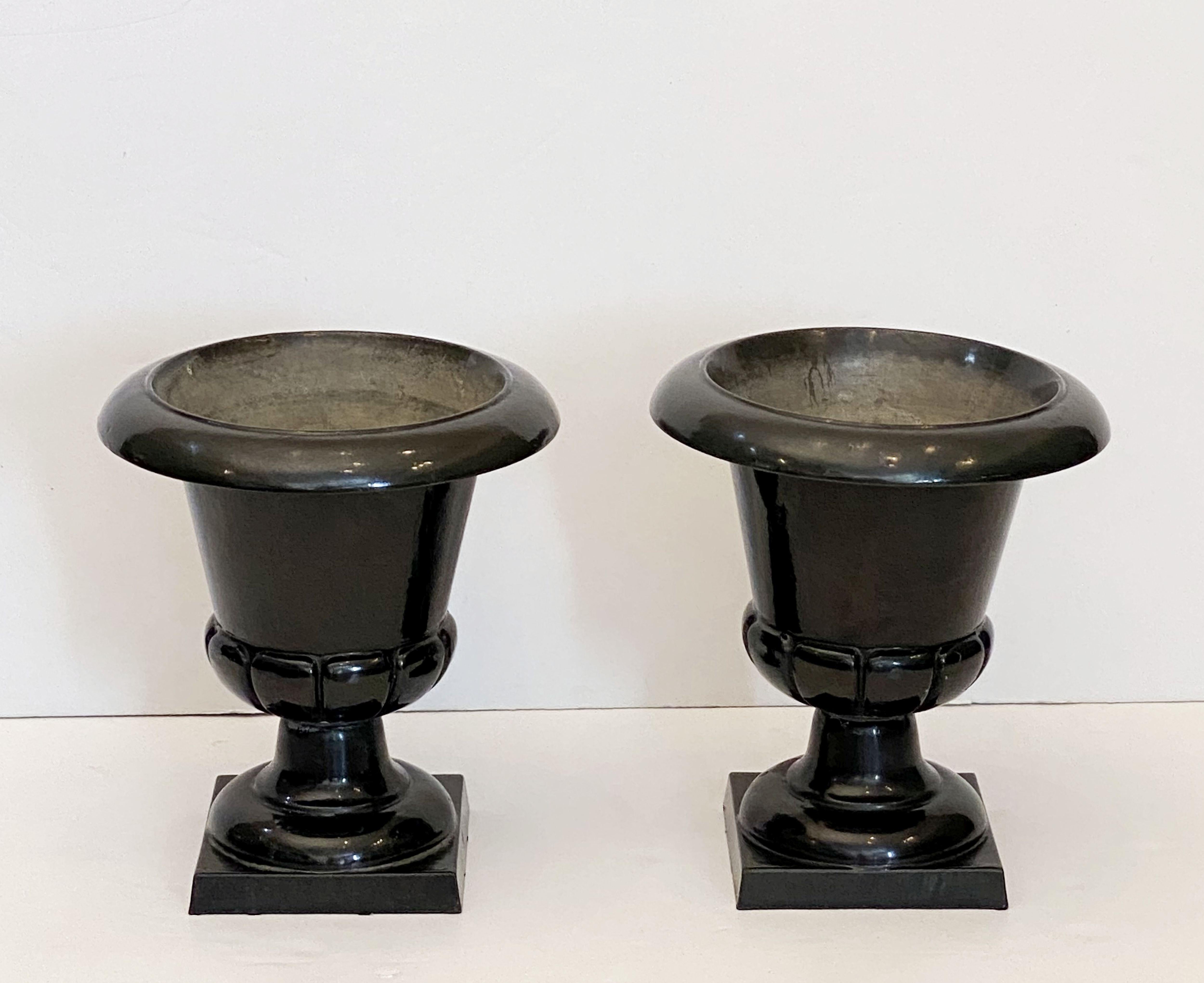 A fine pair of English garden urns or planter pots of cast iron with a black enamel glaze finish, each planter urn resting on a square plinth base.

Perfect for an indoor or outdoor garden room, garden, or conservatory!

Dimensions are height 17 1/2