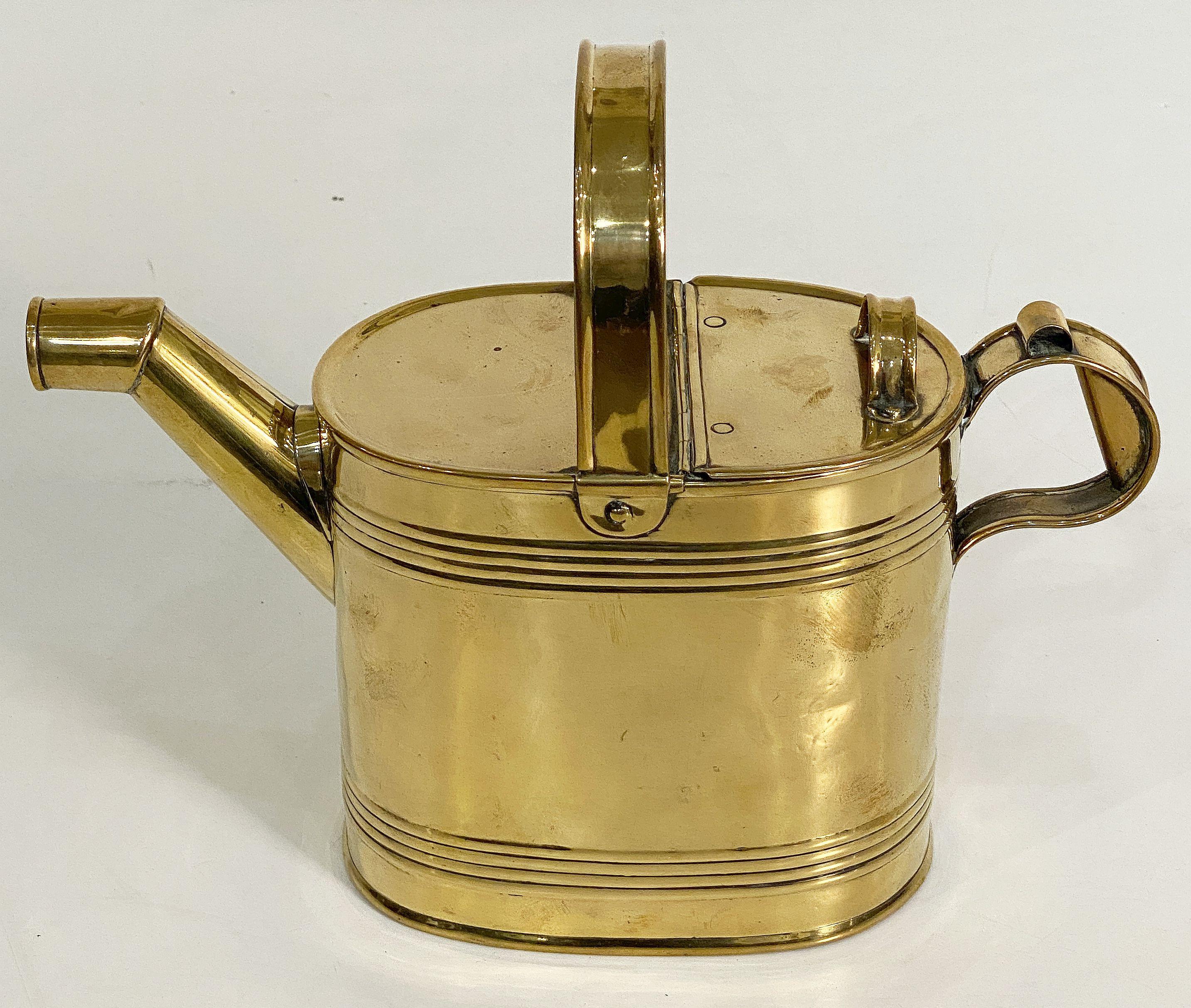 A fine English oval watering can of brass for the garden with a brass handle across the top, hinged back section, and a smaller handle at the end opposite the spout. With registration mark to base.