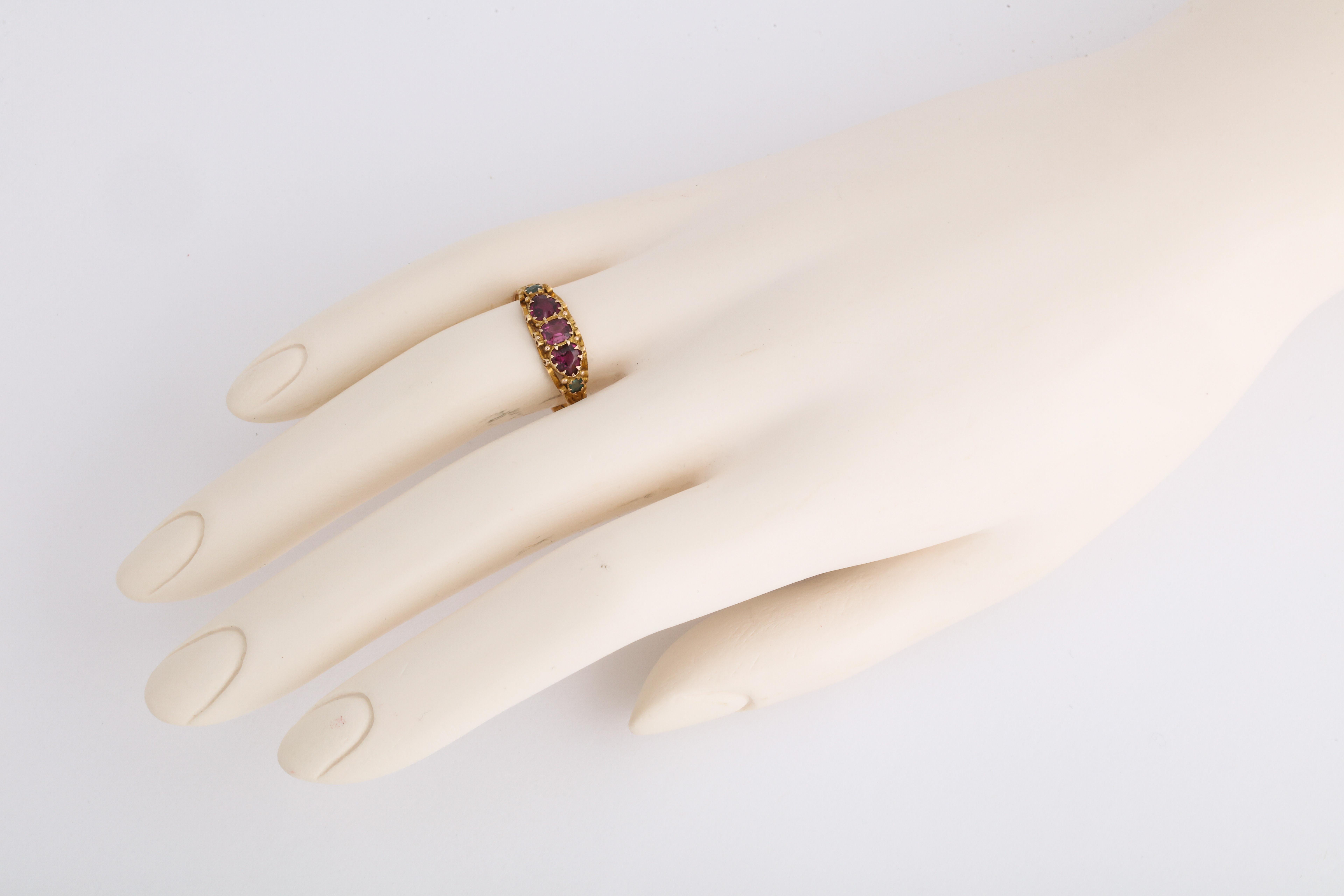 Set with a central oval cut garnet flanked by a heart shaped garnet and a small faceted emerald on each side, mounted in 15kt yellow gold decorated with scrolls and engraved motifs all around the shank, in intact original condition 

England, fully