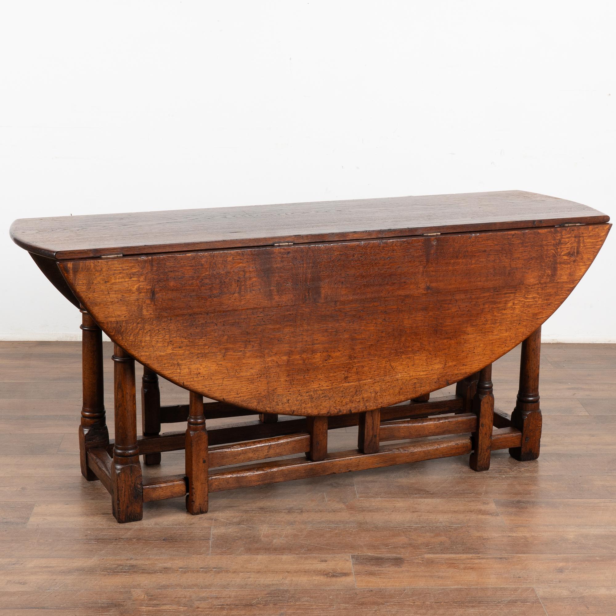 This handsome gateleg dining table is also known as an English wake table with drop leaves.
Notice the dark patina of the oak, aged and naturally distressed over generations of use and lovely turned legs.
The large oval shaped top has 2 drop leaves,