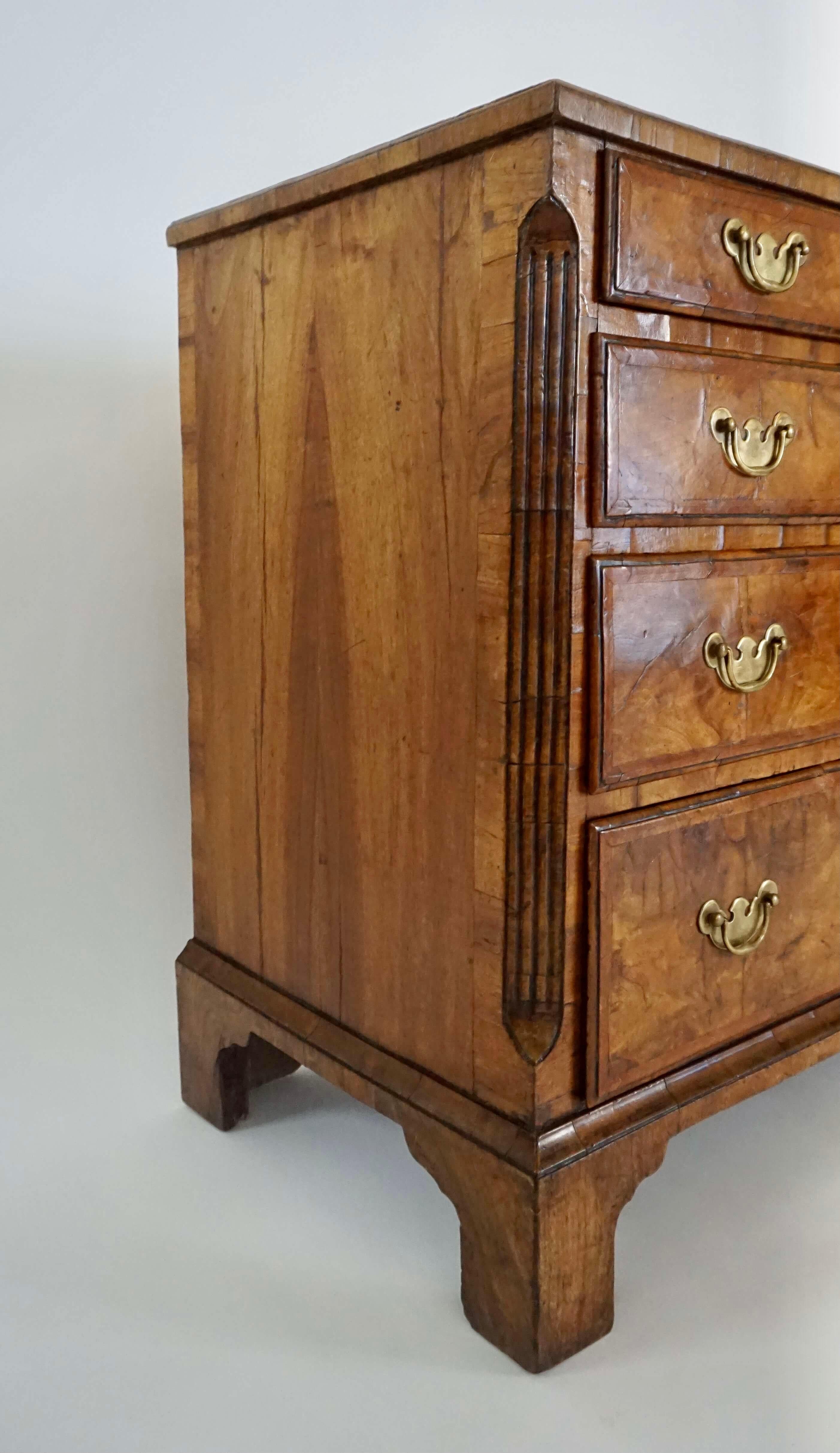 English George I period circa 1725 'bachelor's chest' of four drawers having exquisite flame walnut veneers with brass bail pulls and escutcheons. Key present. Provenance available upon request.