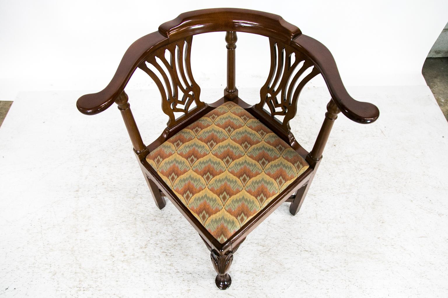 This corner chair has carved open splats. The apron has carved quarter fan brackets. The front legs have a carved stylized shell framed by volutes with single pendant bellflowers. The legs are joined by a cross stretcher. The front leg terminates in